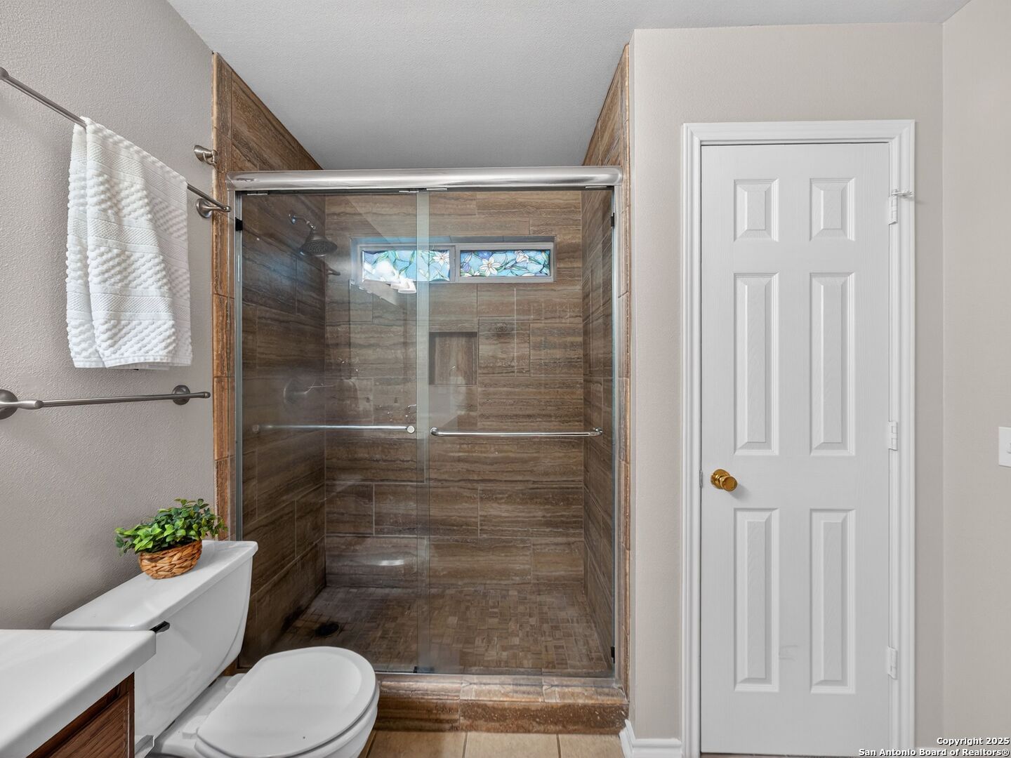 Bathroom with a glass-enclosed brown tile shower and a narrow stained-glass window.