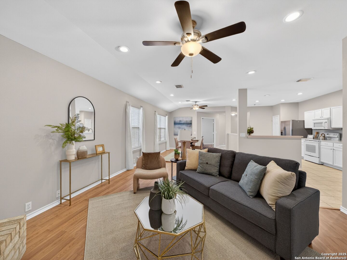 Furnished living room with a dark gray sofa, wood floors, and an open kitchen beyond.
