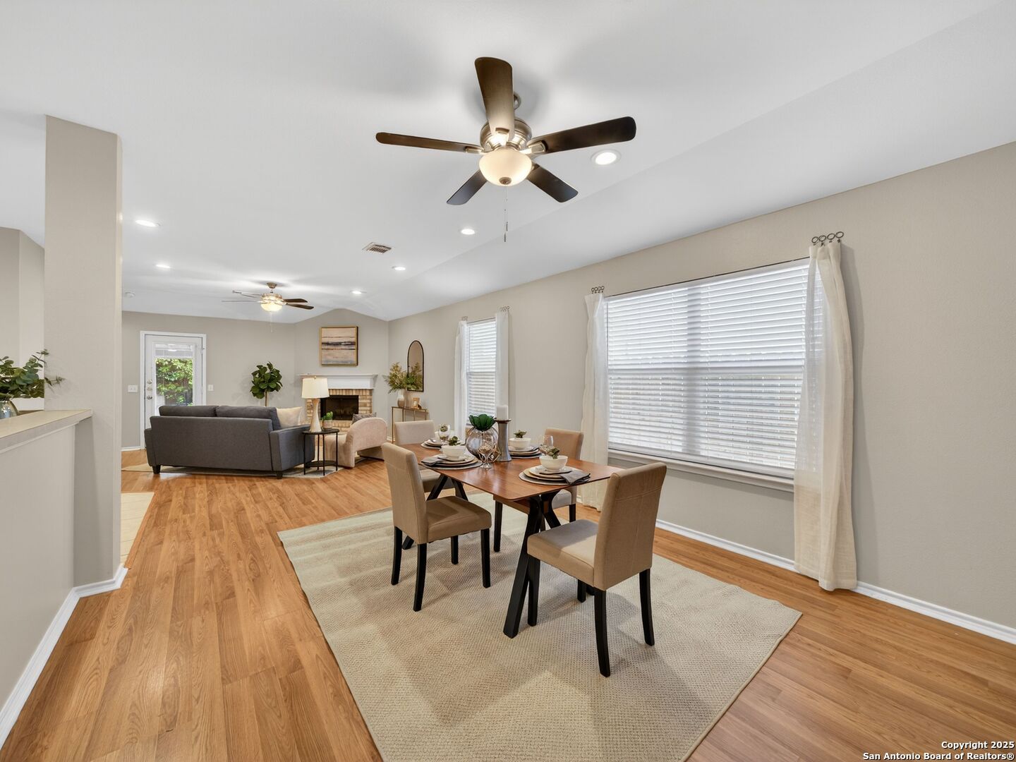 Open-plan dining and living area with a set table, fireplace, and large curtained windows.