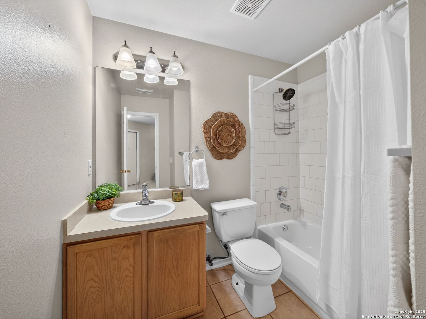 Bathroom with wood vanity, large mirror, and white tiled tub-shower behind a curtain.