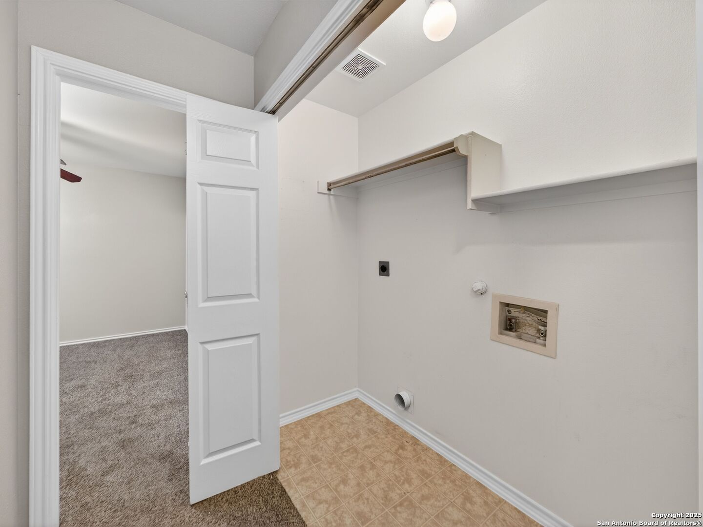 Empty laundry room with tan tile flooring, washer and dryer hookups, and open shelving.