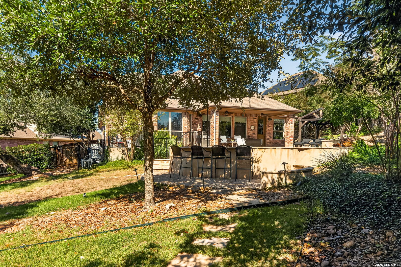 Backyard patio with outdoor seating, mature shade trees, and a brick house with solar panels.