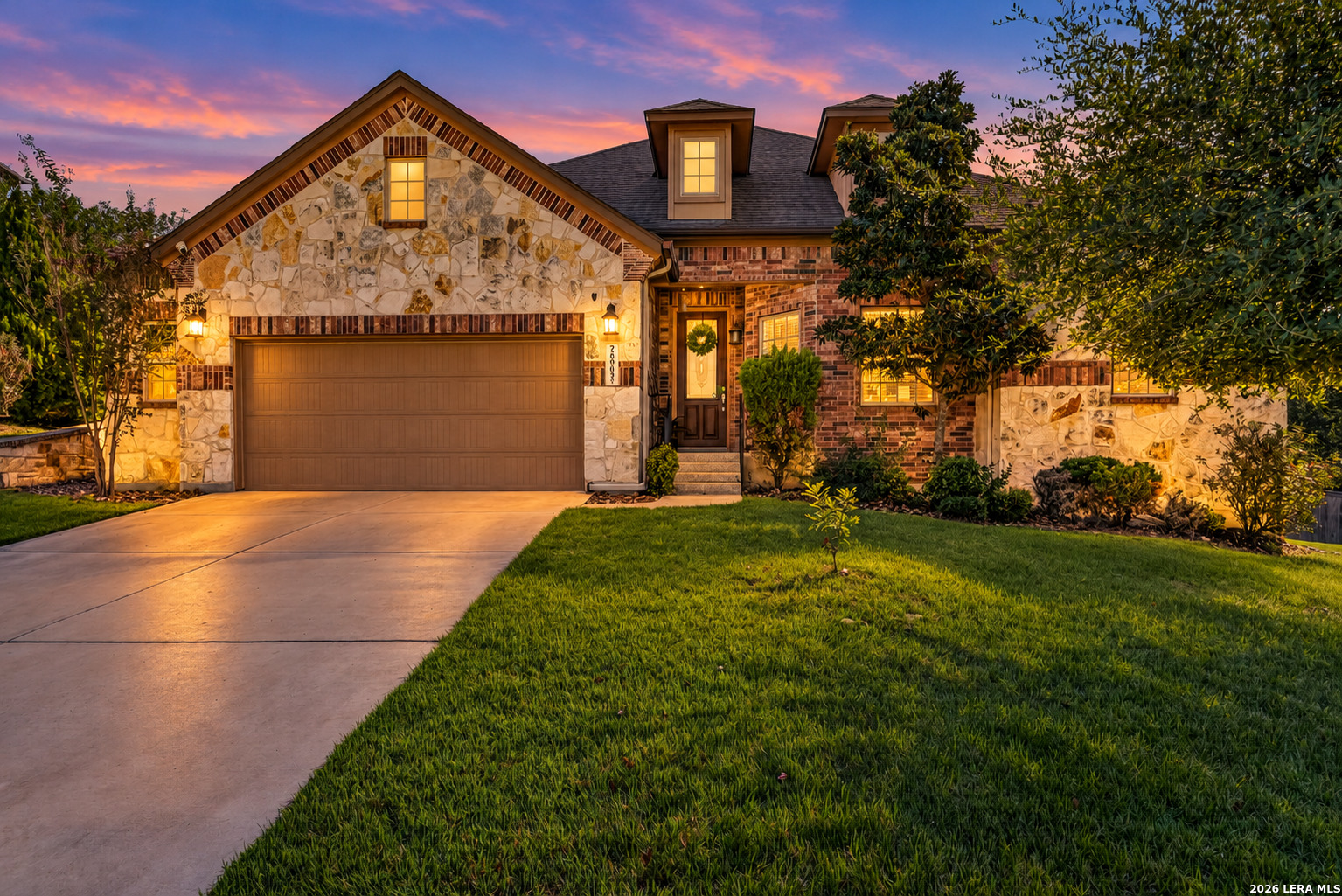 Stone-and-brick home with a double garage and landscaped lawn at sunset.