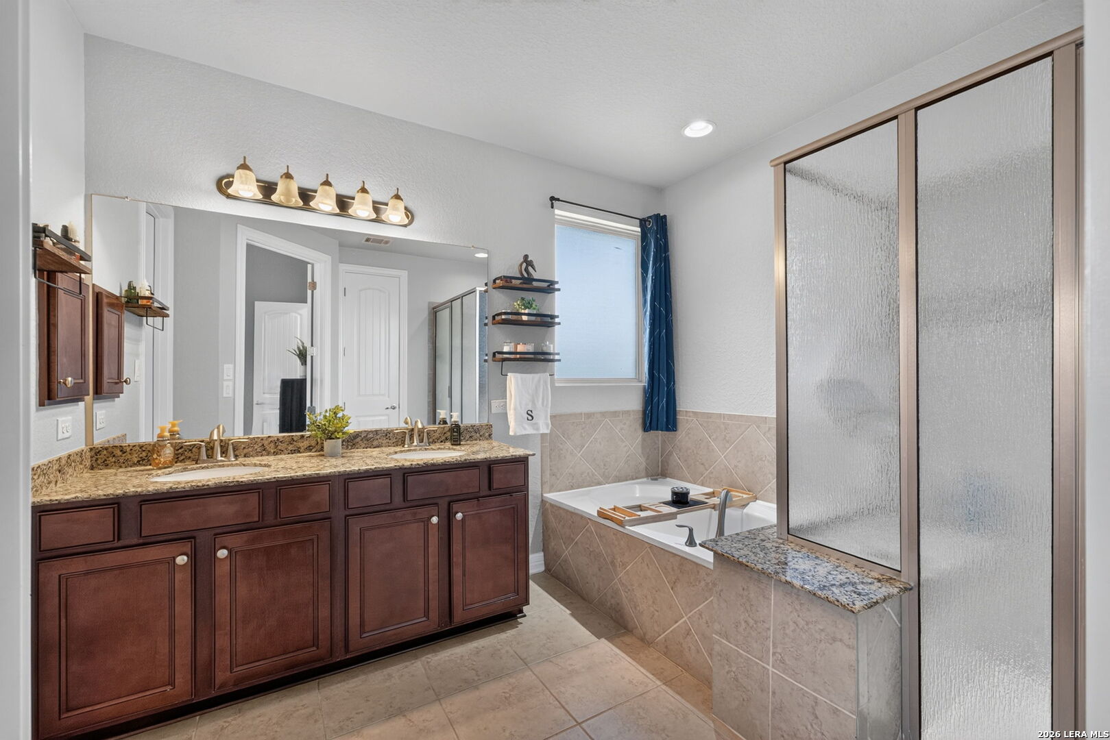 Bathroom with a double-sink vanity, soaking tub, and frosted-glass shower enclosure.