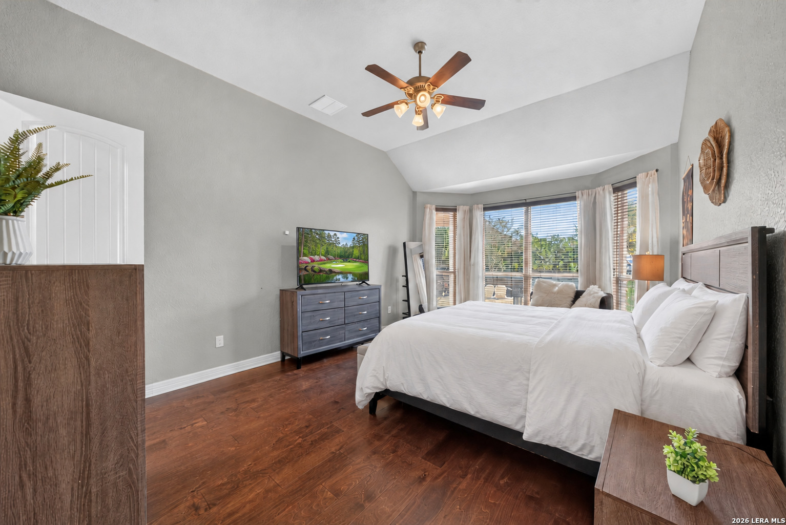 Furnished bedroom with a large bed, hardwood floors, and a bay of curtained windows.