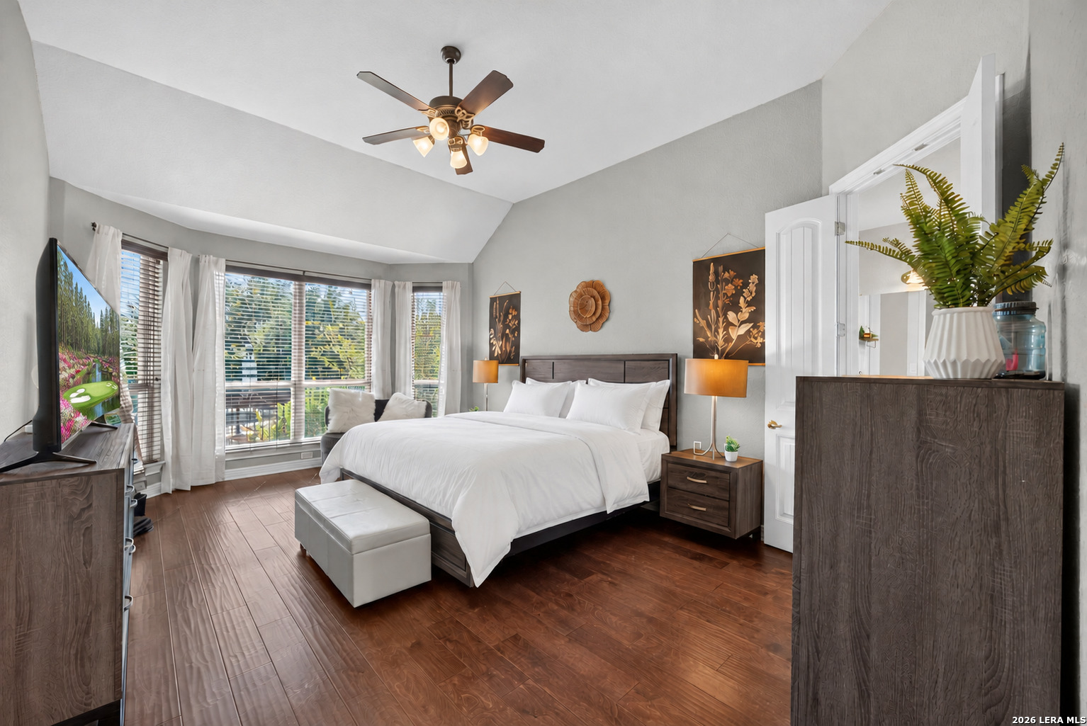 Bedroom with a dark wood bed, white bedding, and large windows overlooking greenery.