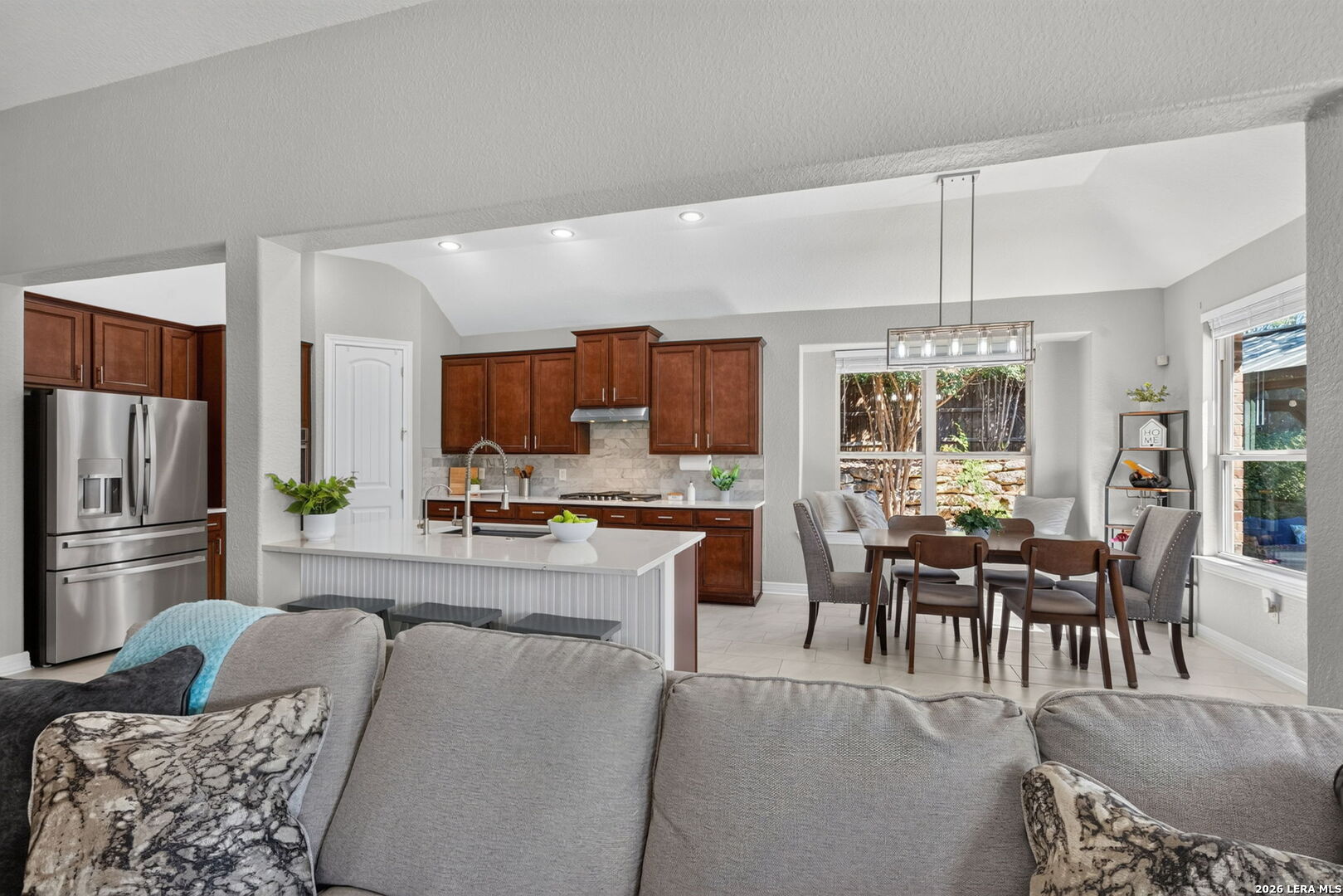 Open kitchen and dining area with dark wood cabinets, an island, and a stainless steel refrigerator.