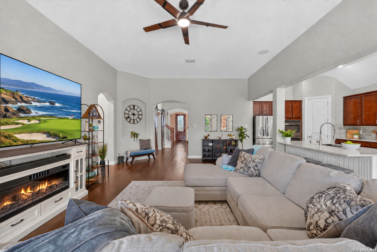 Furnished living room with a fireplace, large sectional, ceiling fan, and open kitchen.