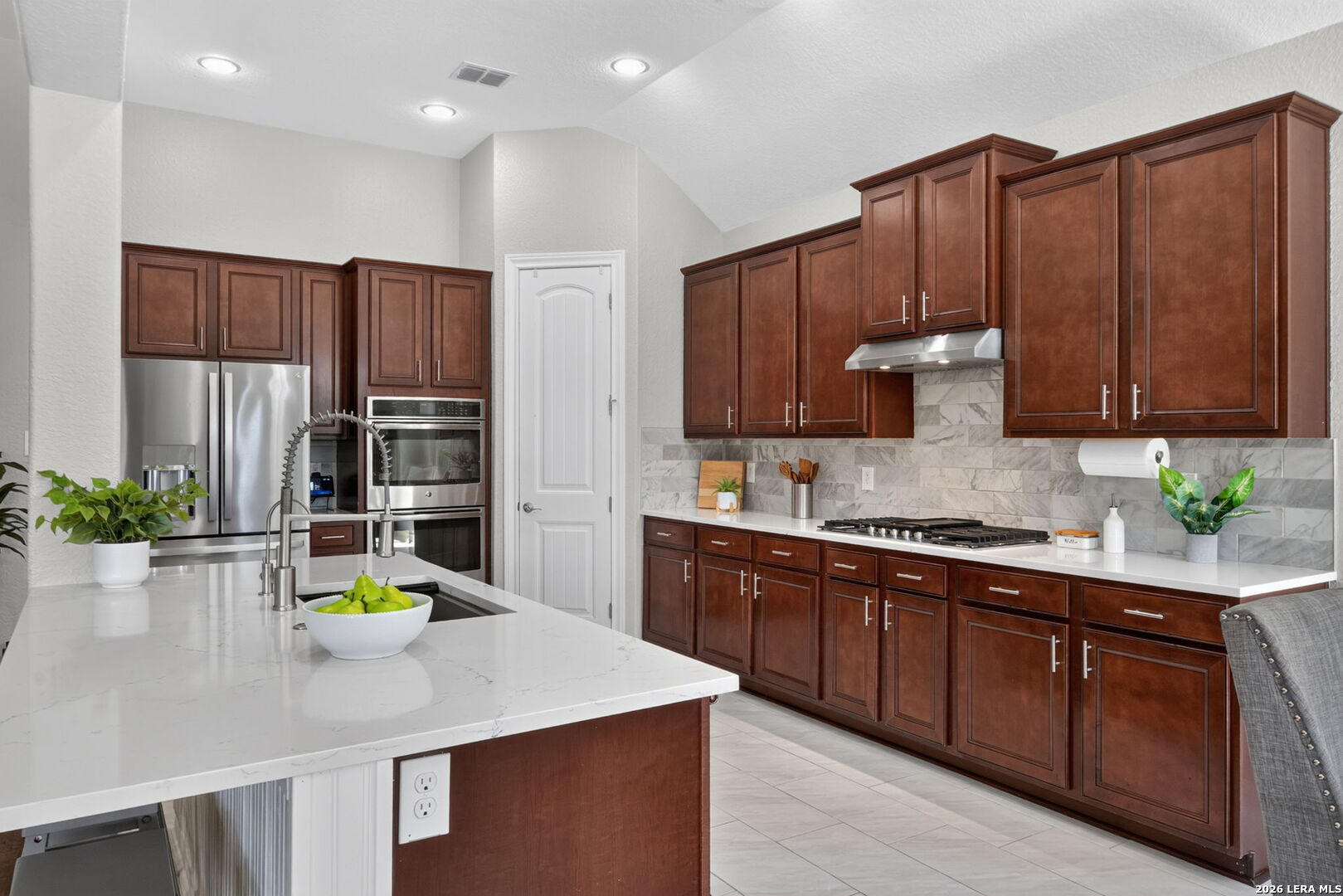 Kitchen with dark wood cabinets, marble backsplash, stainless steel appliances, and a large island.