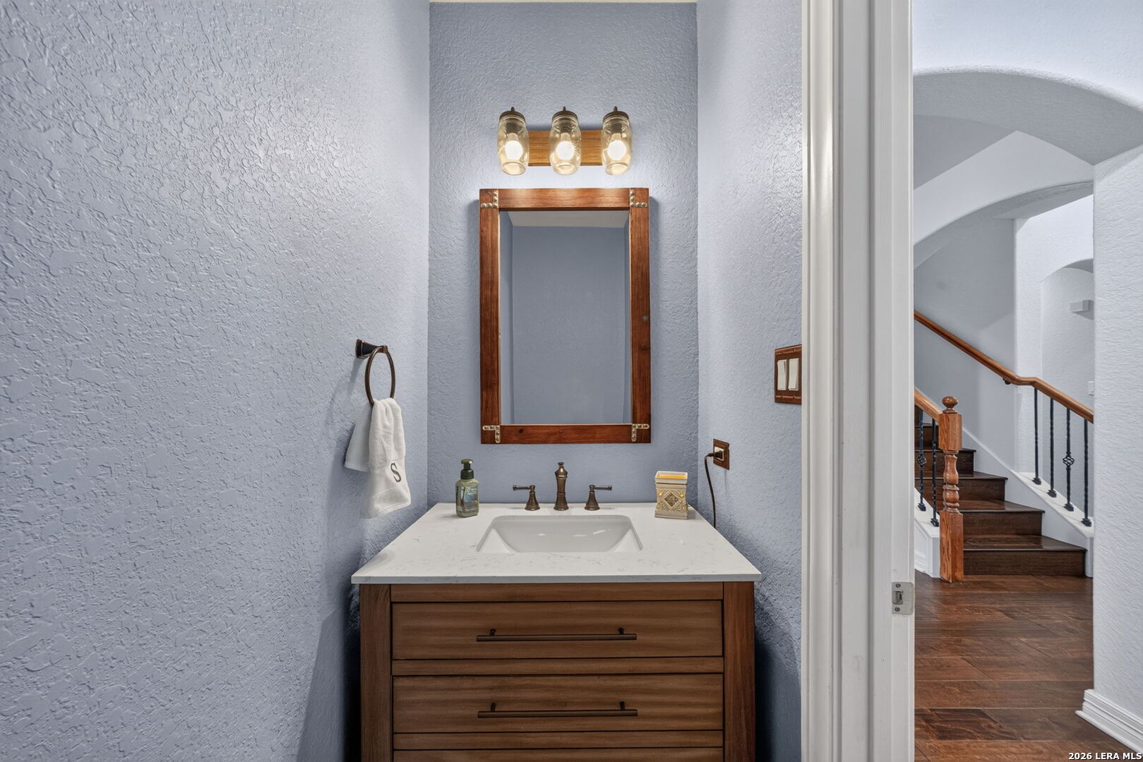 Bathroom vanity with a wood-framed mirror and three-light fixture beside the staircase.