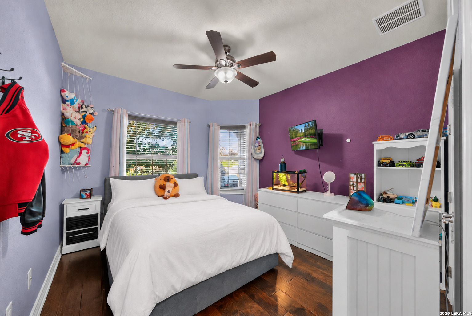 Bedroom with a white bed, purple accent wall, ceiling fan, and dresser with aquarium.