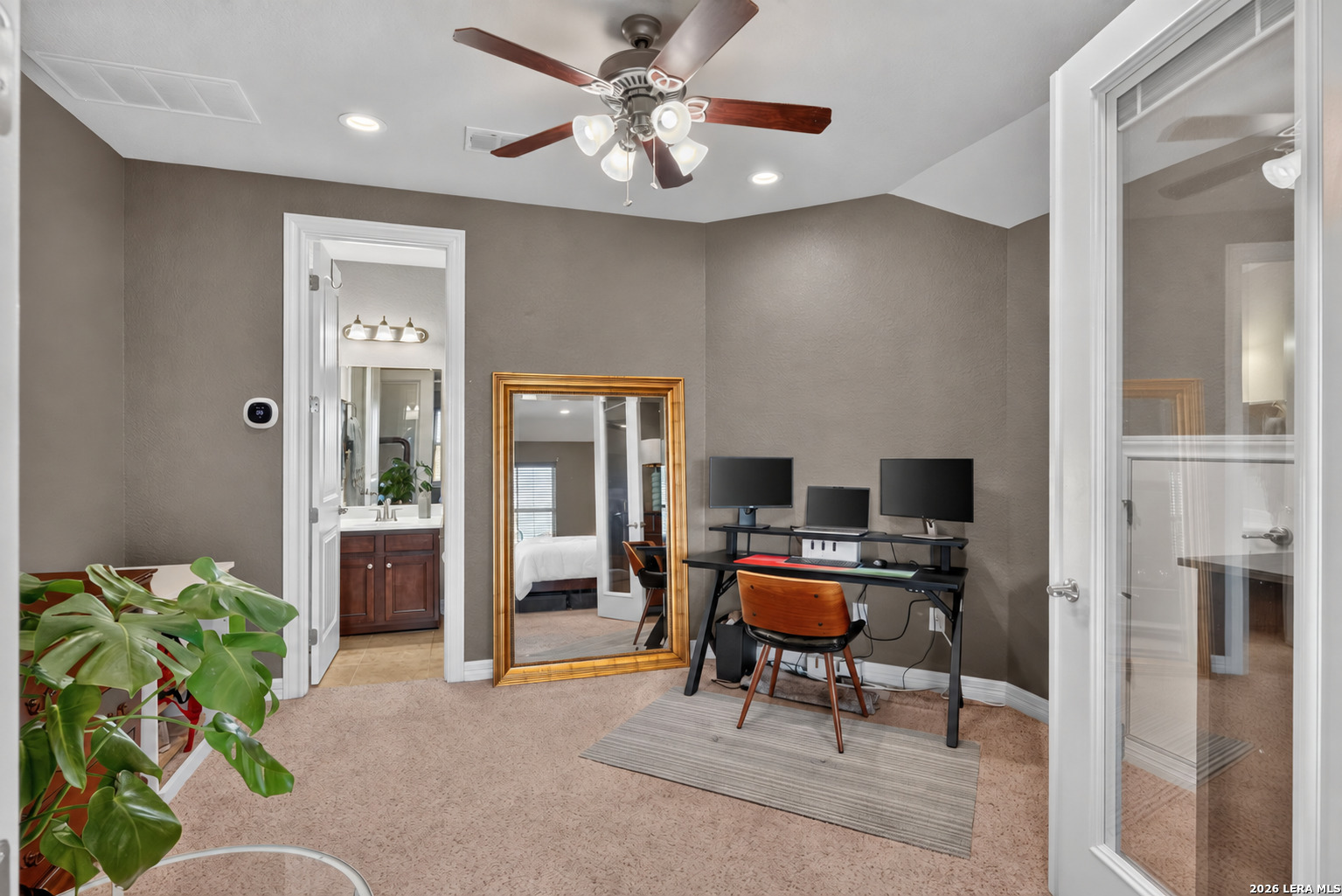 Home office with a three-monitor workstation, ceiling fan, and a full-length mirror.