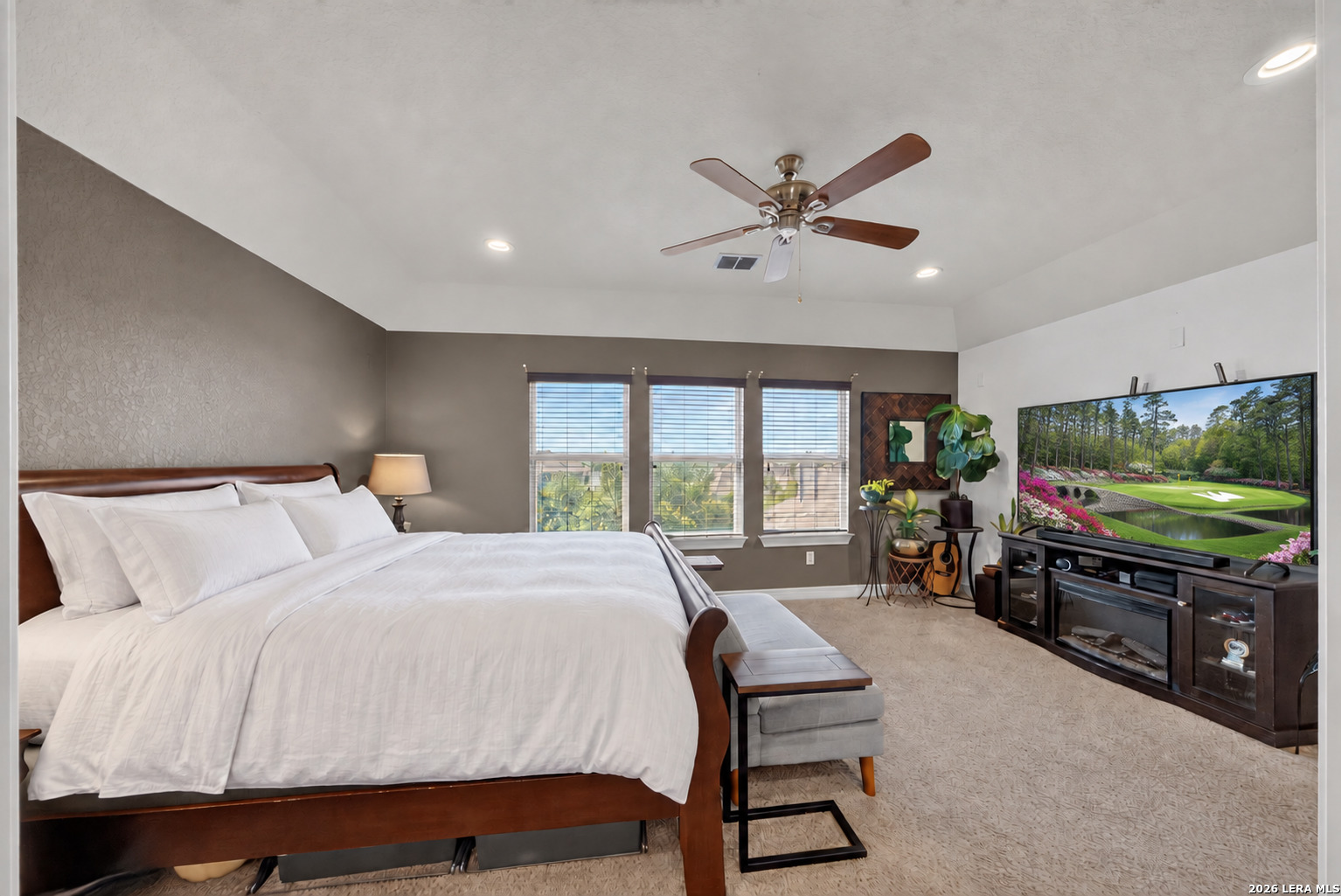 Furnished bedroom with a large wooden bed, three windows, and a ceiling fan.