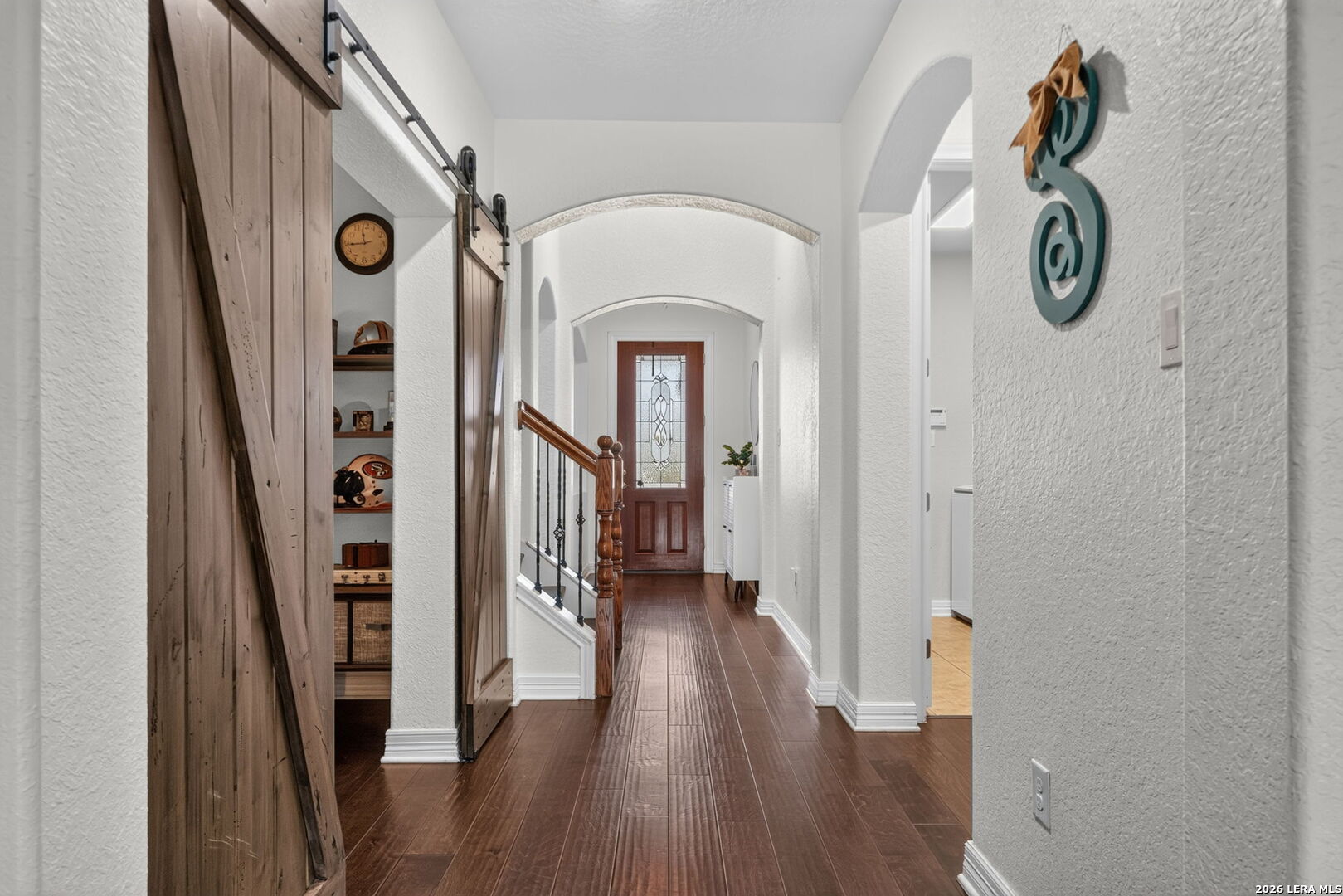 Bright entry hallway with dark wood floors, sliding barn doors, and arched openings.