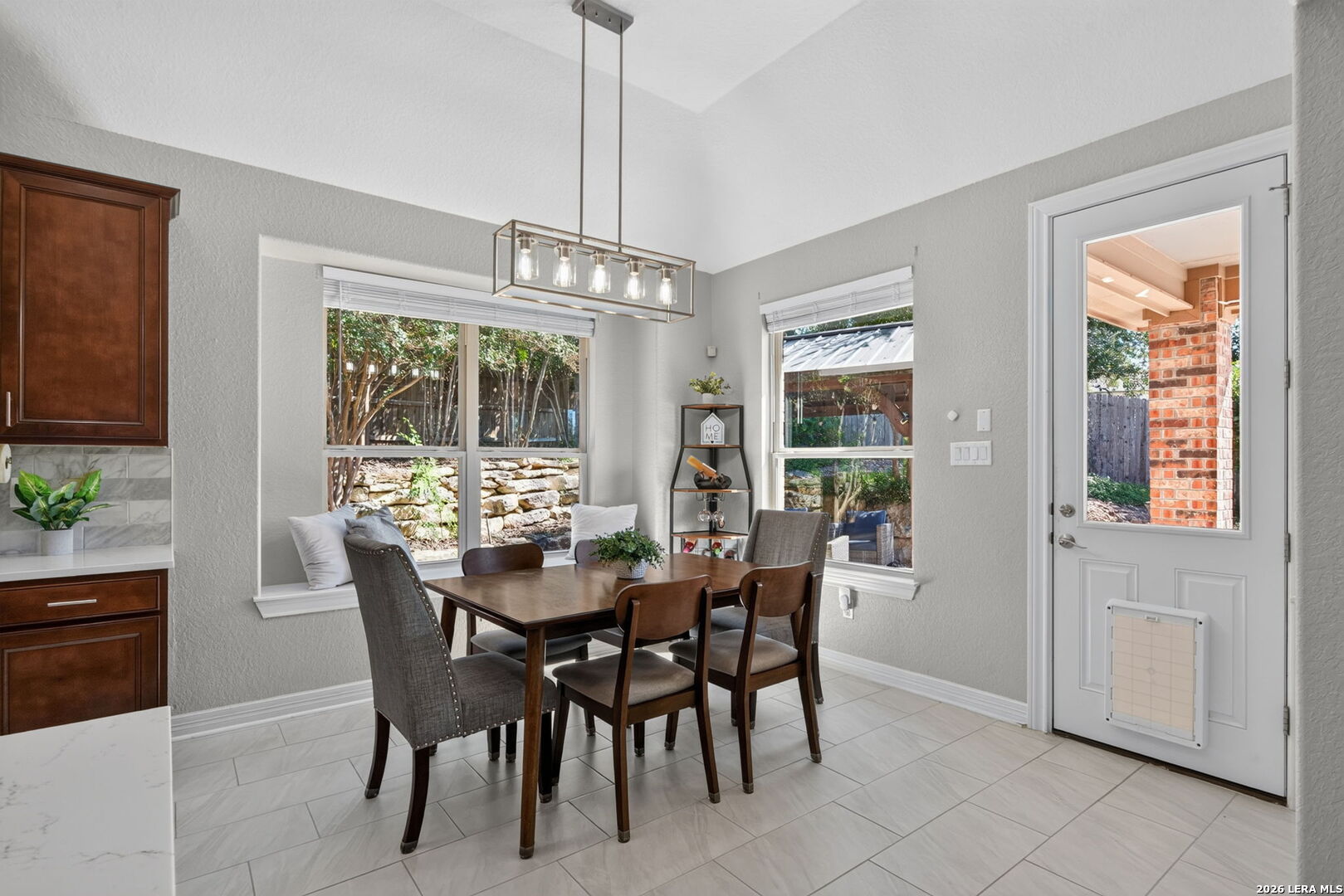Dining area with a wood table, large windows, and a door opening to the backyard.