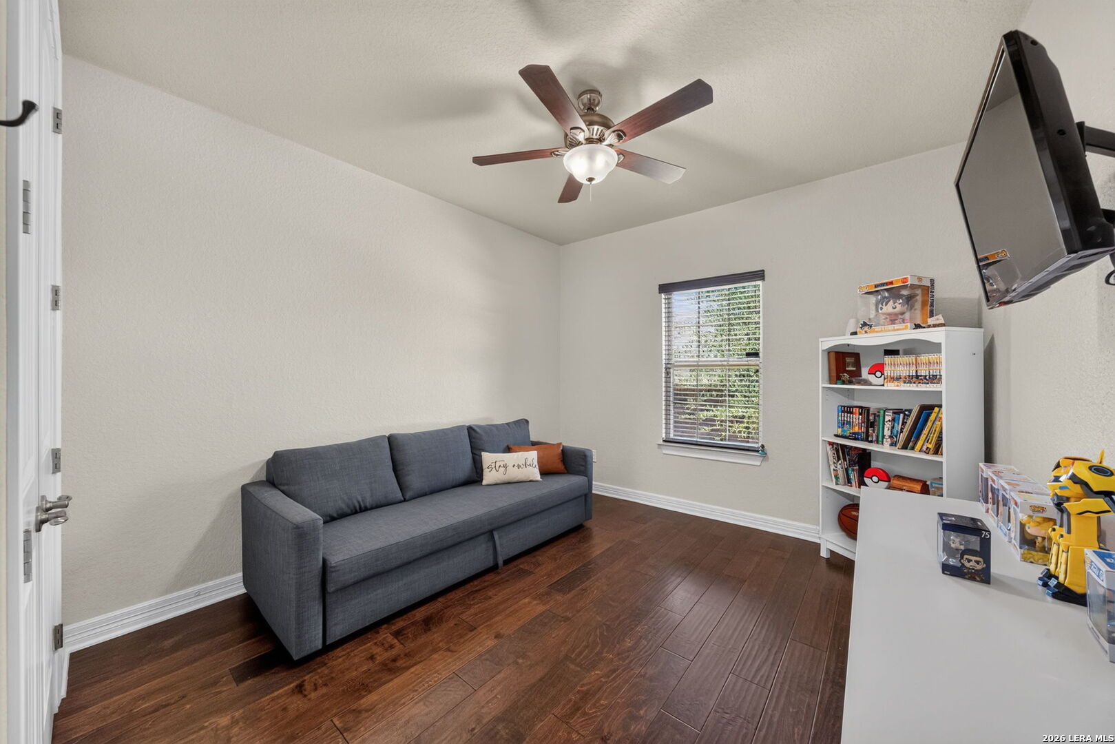 Furnished game room with a gray sofa, wall-mounted television, and collectible-filled bookshelf.