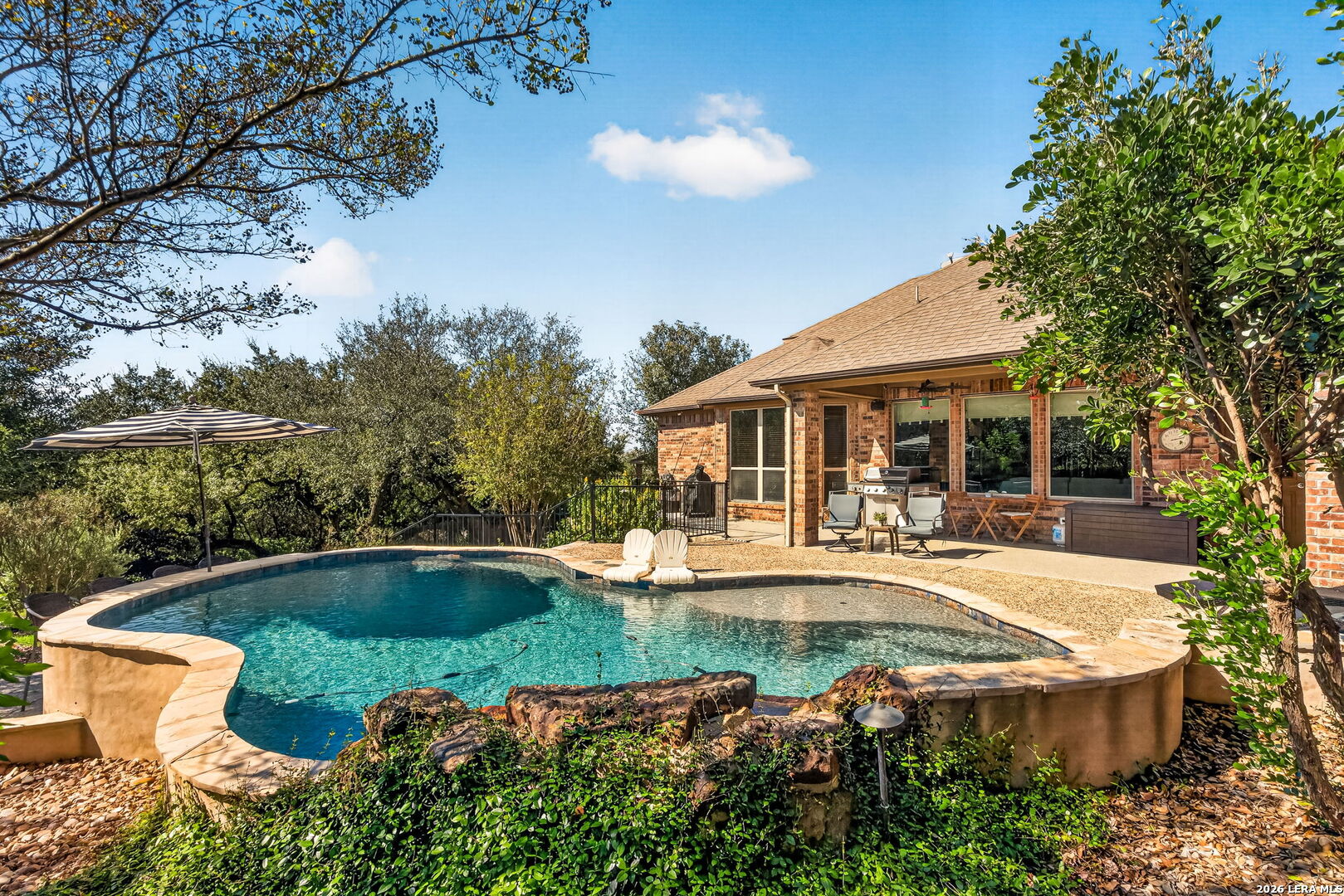 Backyard pool beside a brick home, with a covered patio and outdoor seating.