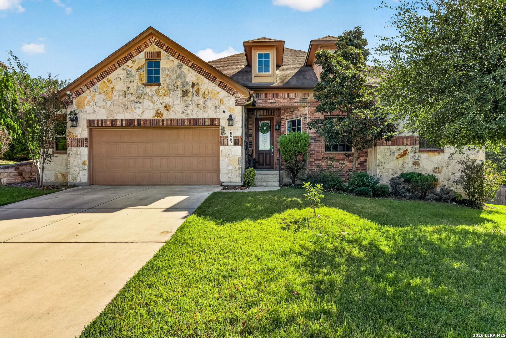 Stone-and-brick home with a two-car garage, broad driveway, and green front lawn.