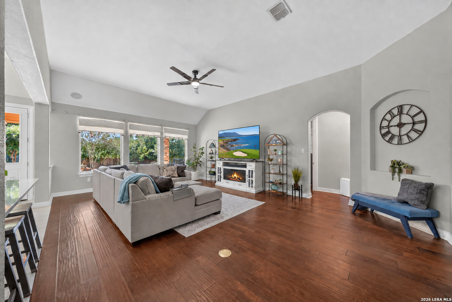 Living room with a fireplace, gray sectional, large windows, and dark wood flooring.