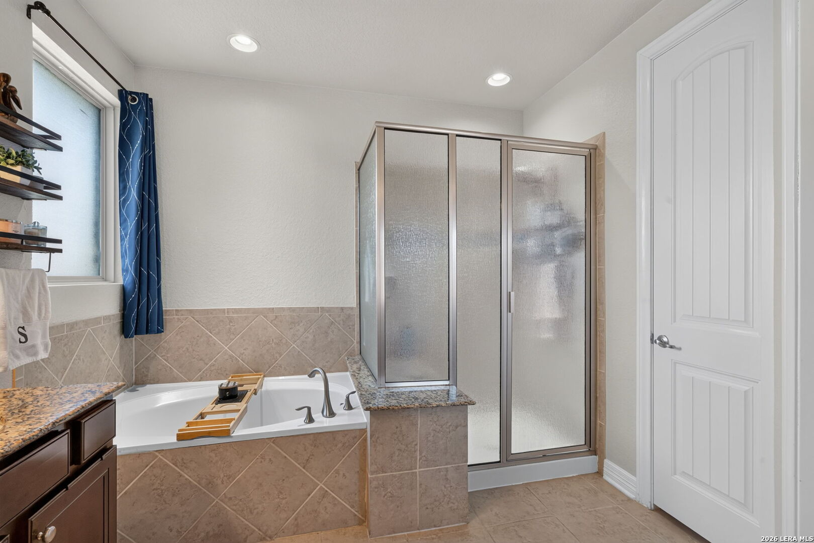 Bathroom with a soaking tub beside a frosted-glass shower and granite vanity.