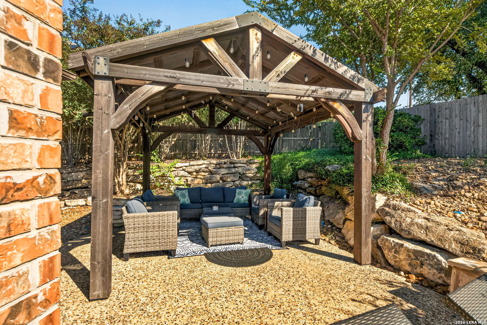 Backyard patio with a timber pergola, string lights, and outdoor lounge seating.