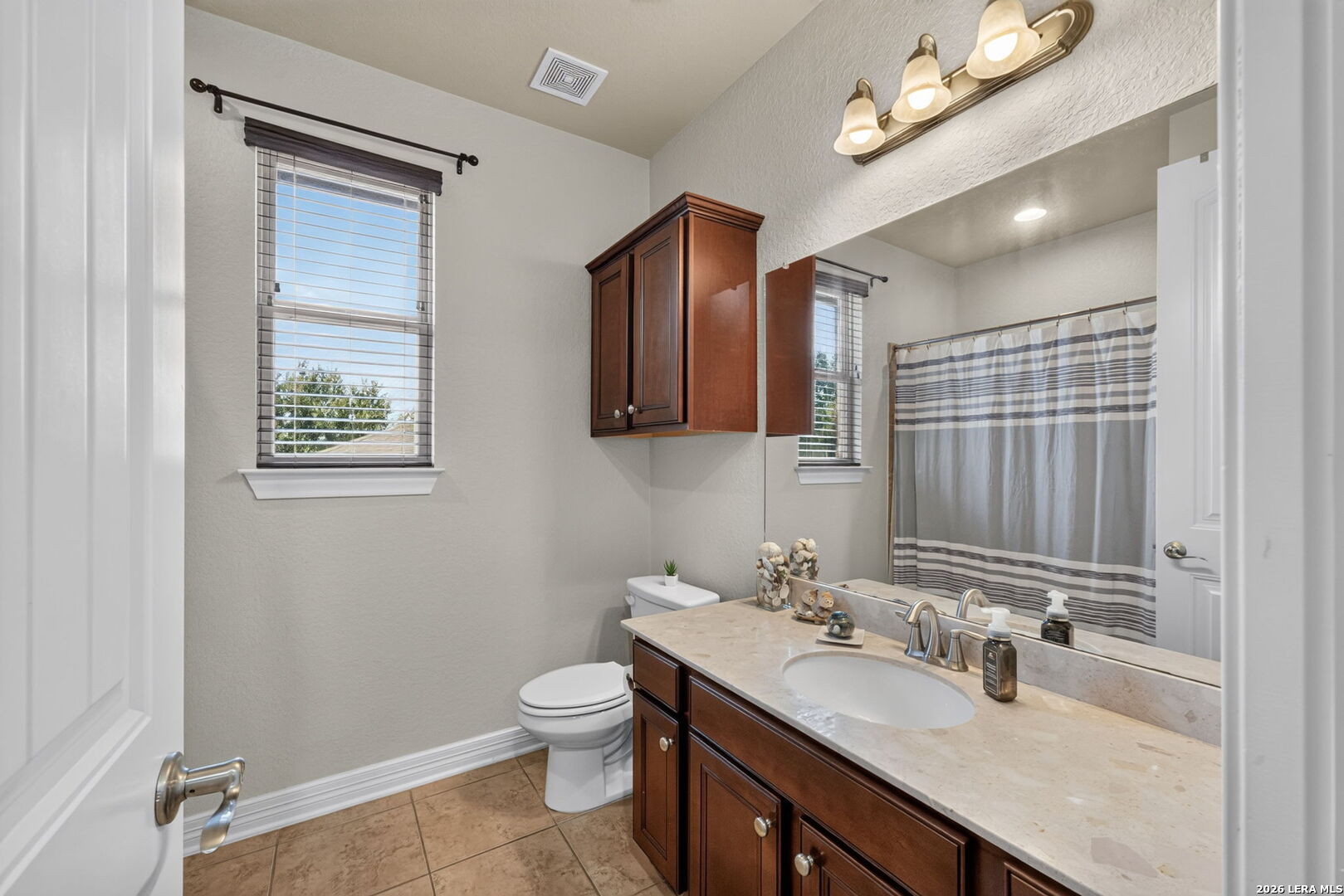 Bathroom with a long wood vanity, large mirror, window, and striped shower curtain.