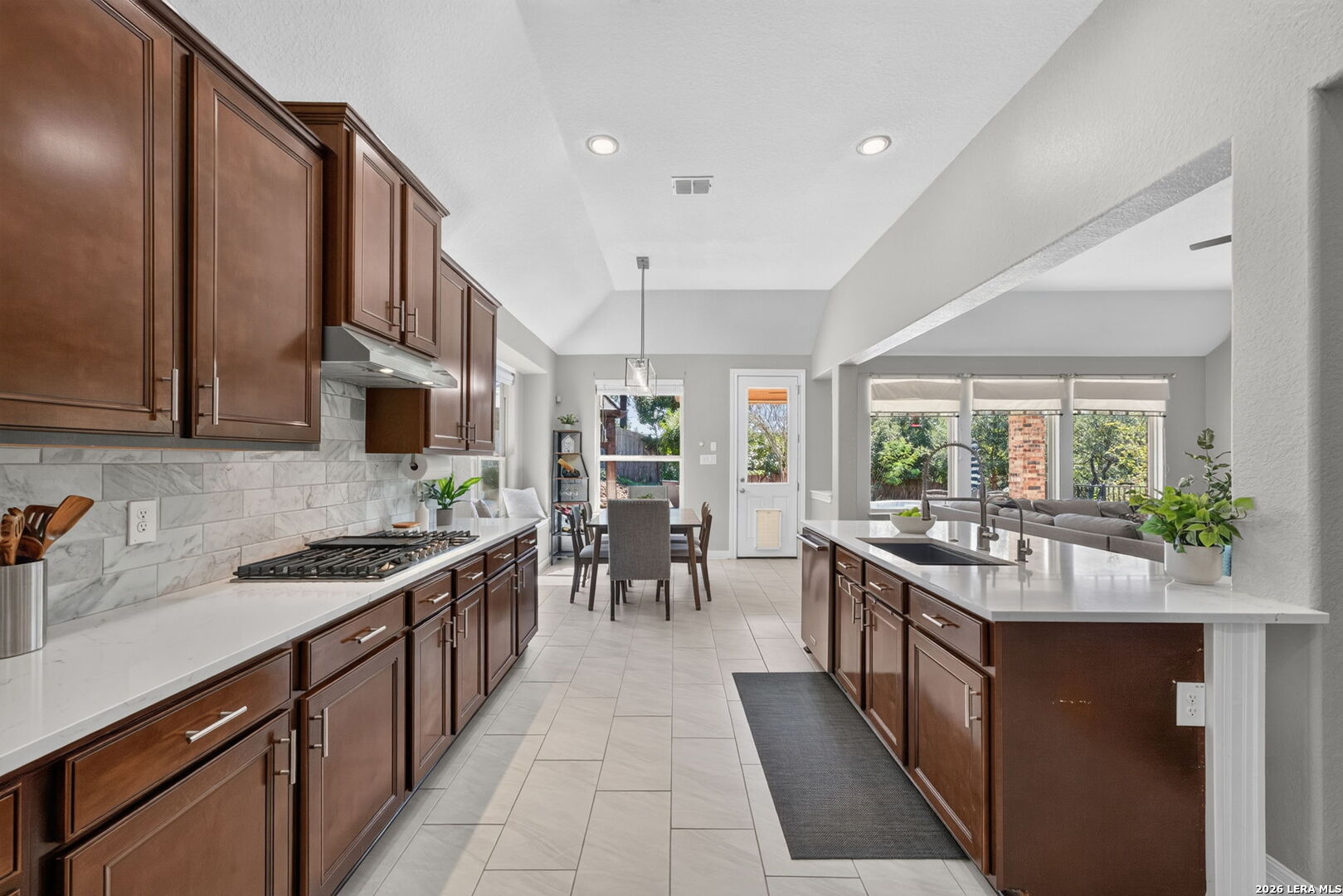 Kitchen with dark wood cabinets, a marble backsplash, and a large island opening to the dining and living areas.