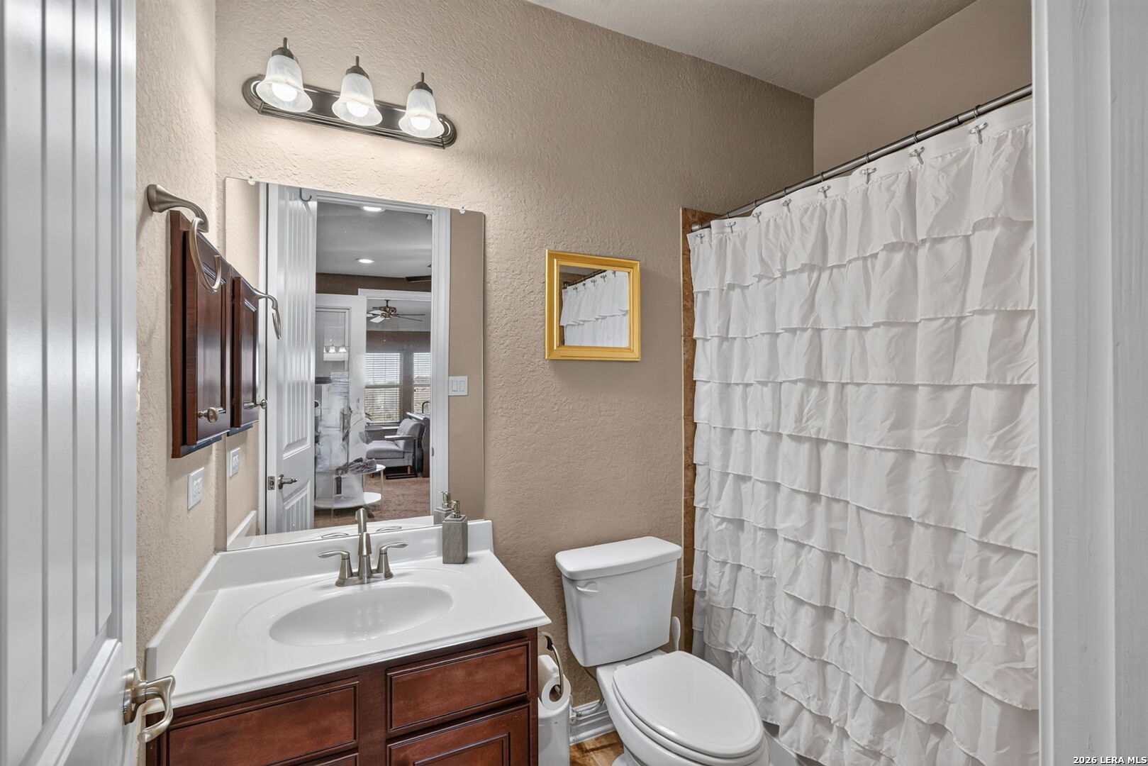 Bathroom with a dark wood vanity, white ruffled shower curtain, and toilet.