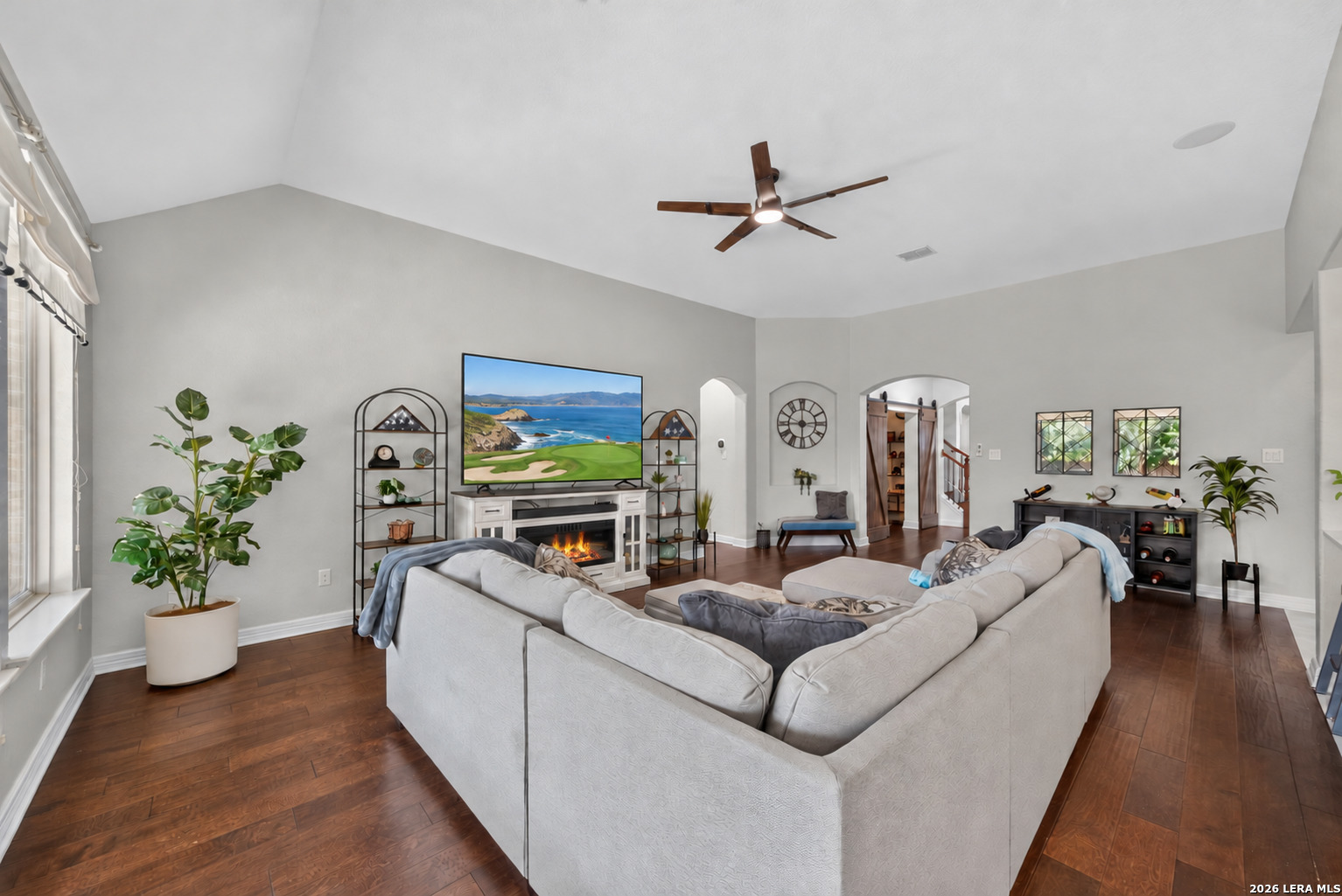 Furnished living room with a vaulted ceiling, white sectional, fireplace, and large television.