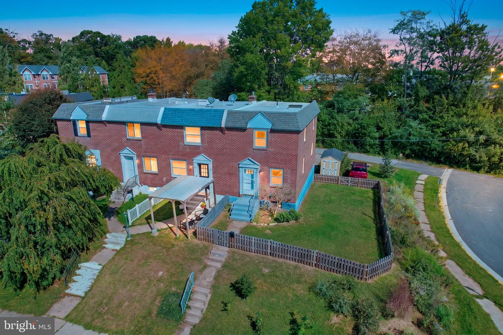 Aerial view of red-brick townhomes with fenced yards beside a curved street.