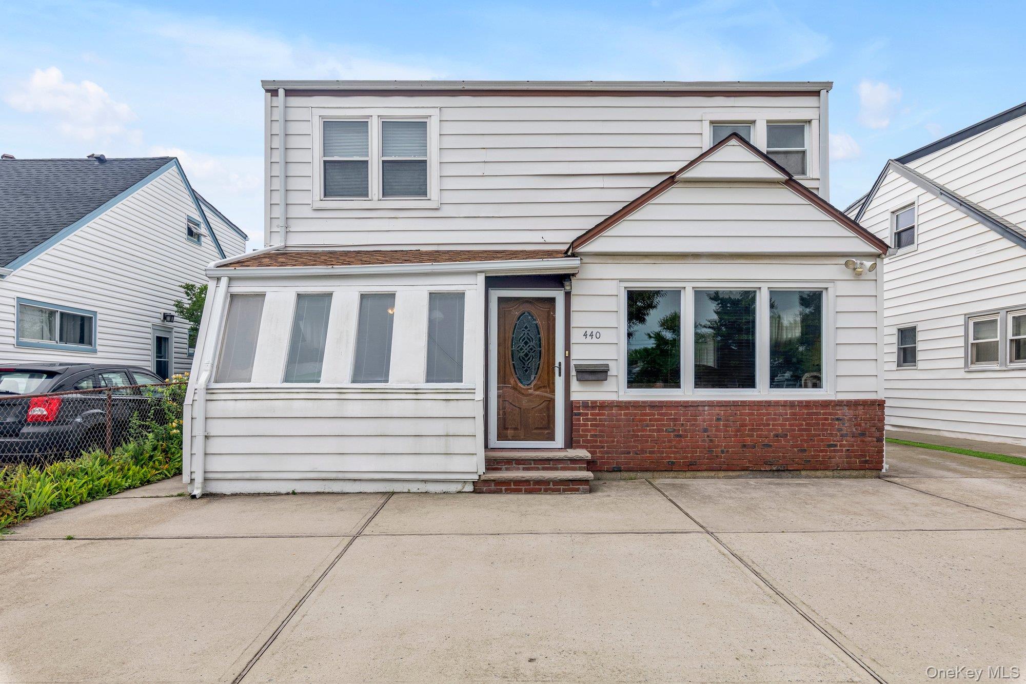 White two-story house with a brick facade, enclosed porch, and decorative wooden front door.