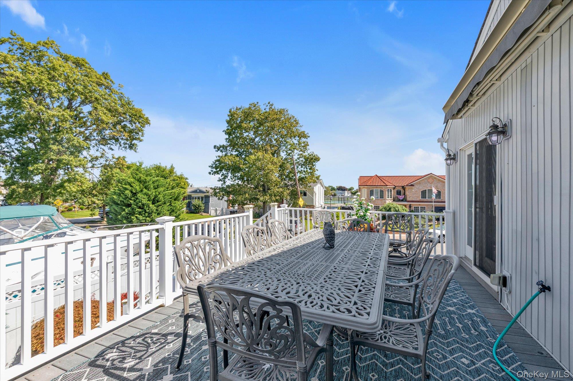 Furnished deck with a large dining table overlooking a boat and neighboring homes.