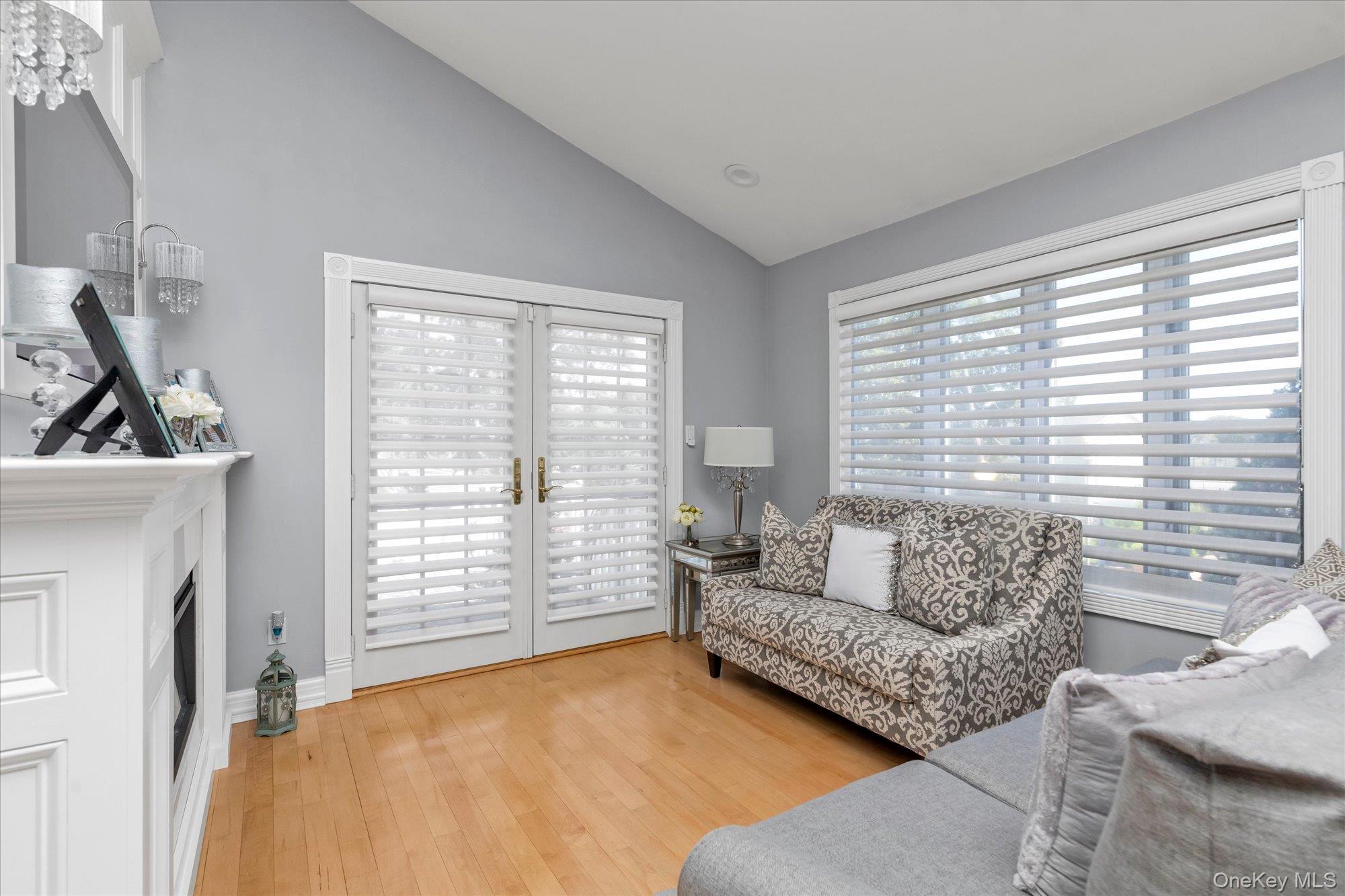 Living room with a white fireplace, shuttered French doors, patterned loveseat, and large windows.