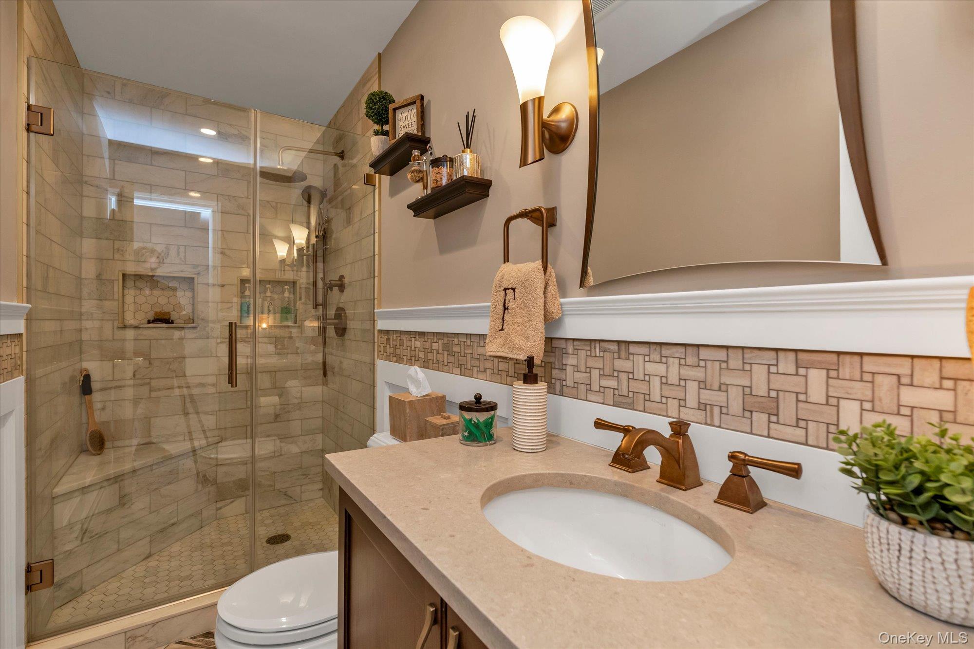 Bathroom with a glass-enclosed marble-look shower and a stone vanity with bronze fixtures.