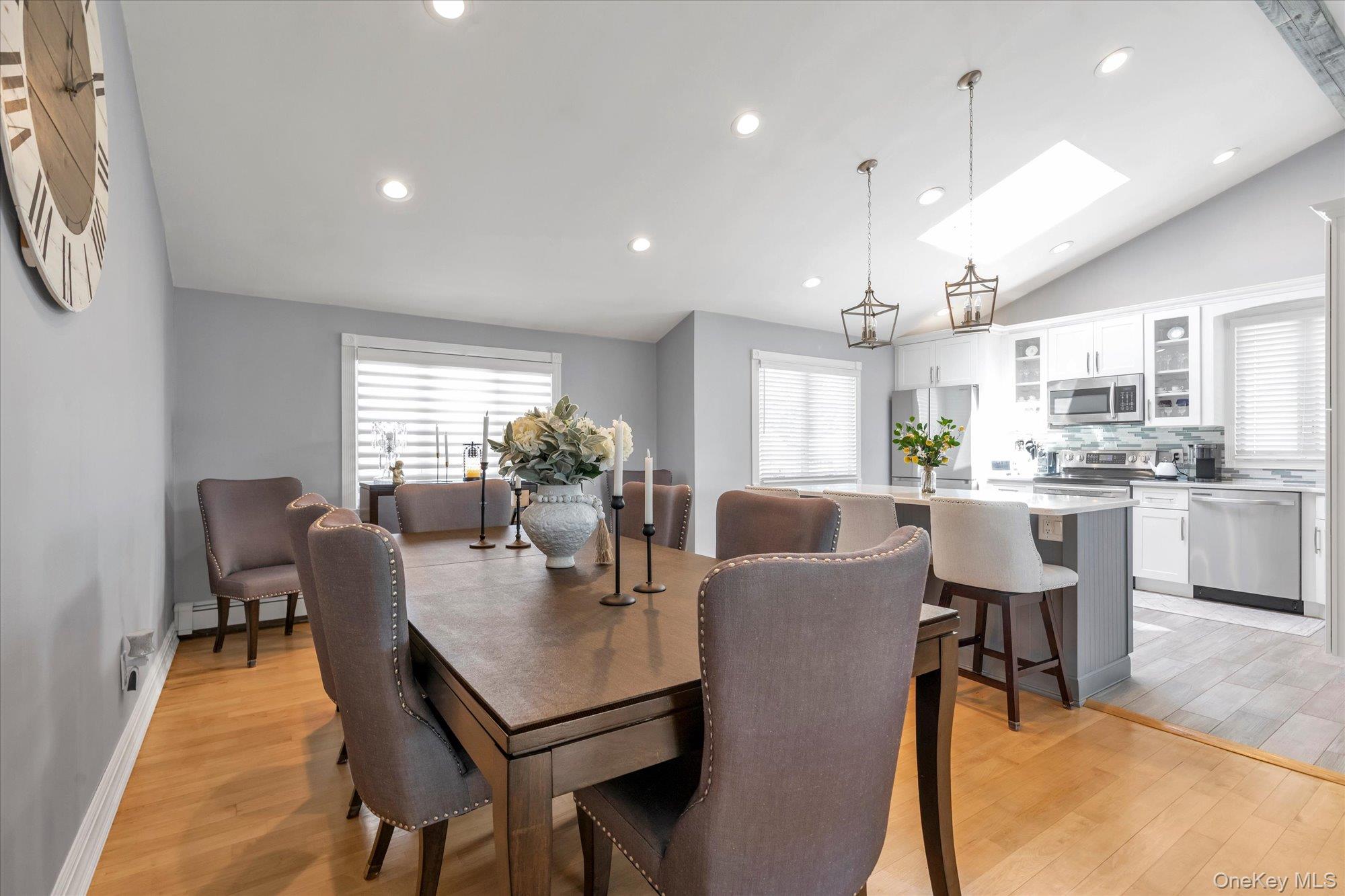 Dining room with a large wood table beside a bright kitchen with an island and skylight.