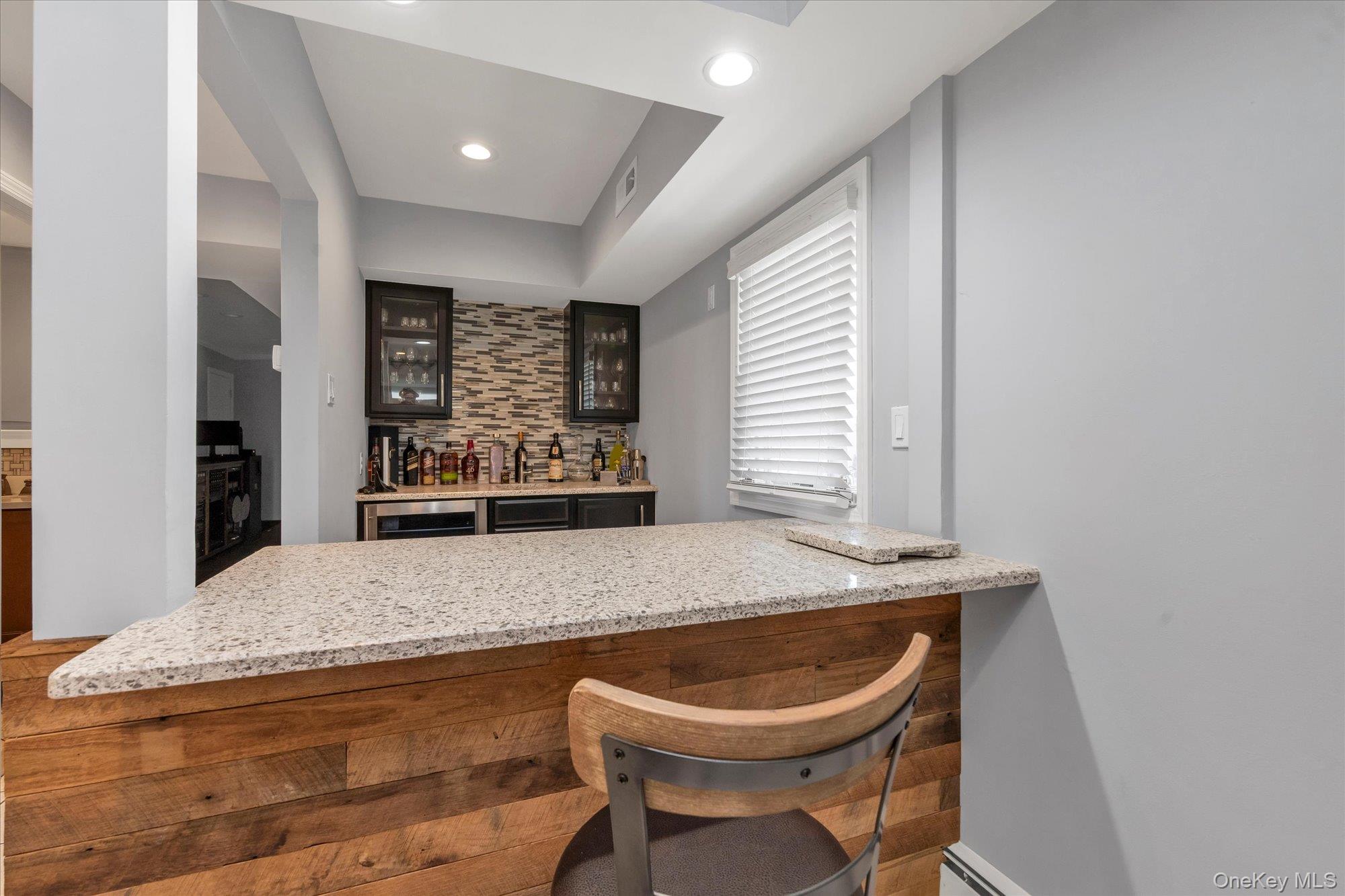 Interior bar with a granite counter, wood-paneled island, dark cabinets, and mosaic tile backsplash.