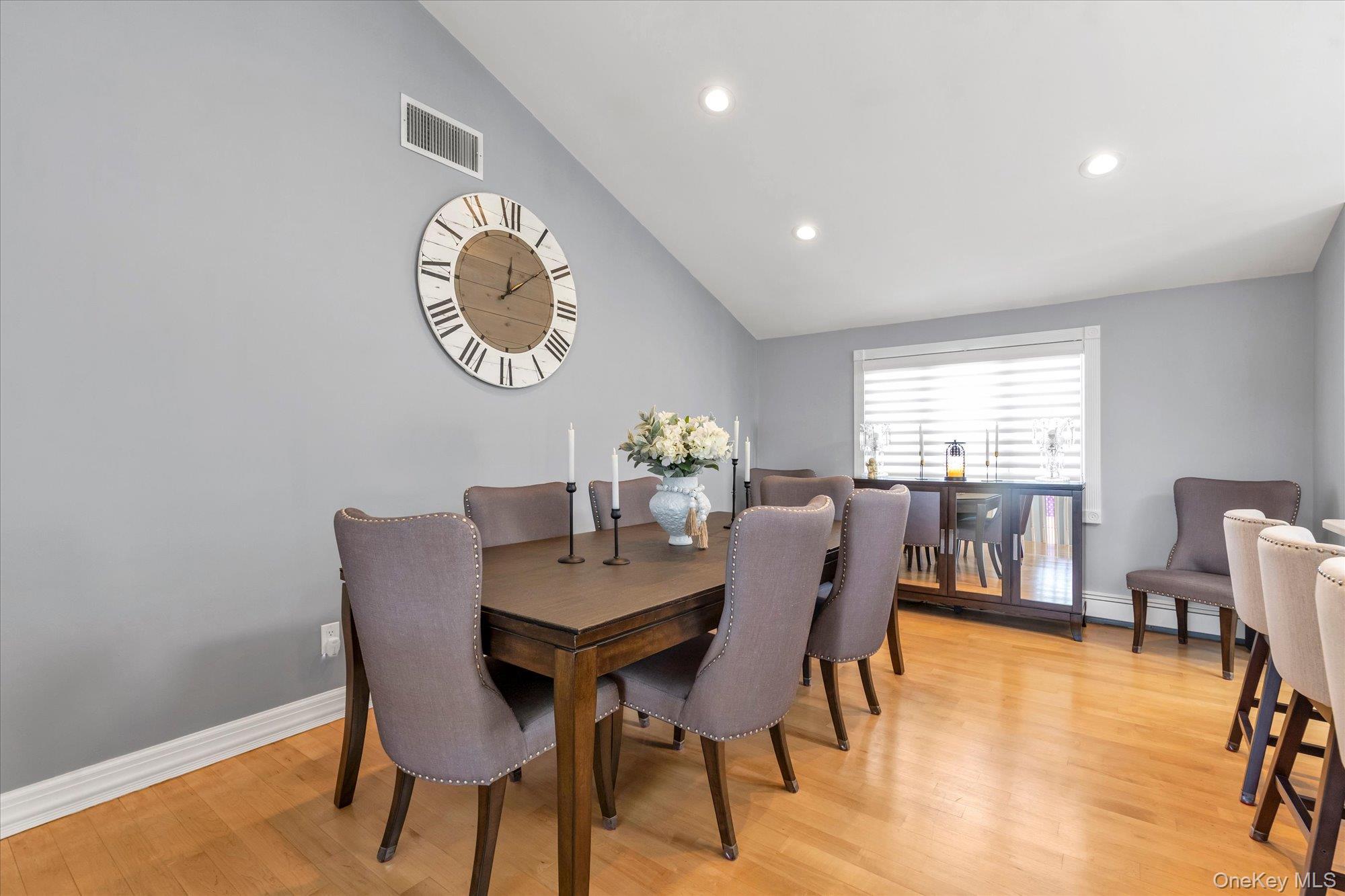Dining room with a dark wood table, upholstered chairs, hardwood floors, and a large wall clock.