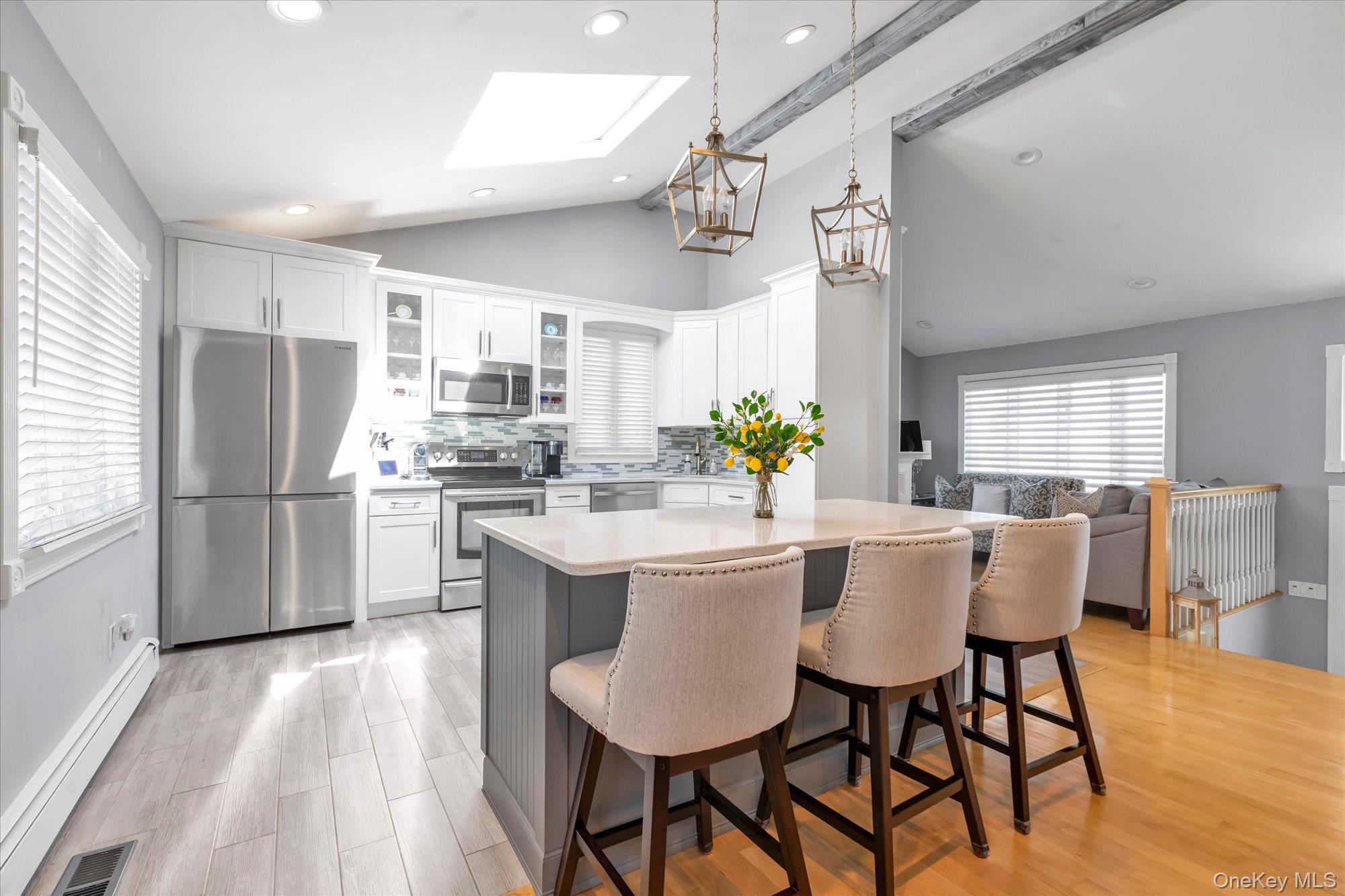 Bright kitchen with a large island, three bar stools, white cabinetry, stainless appliances, and a skylight.