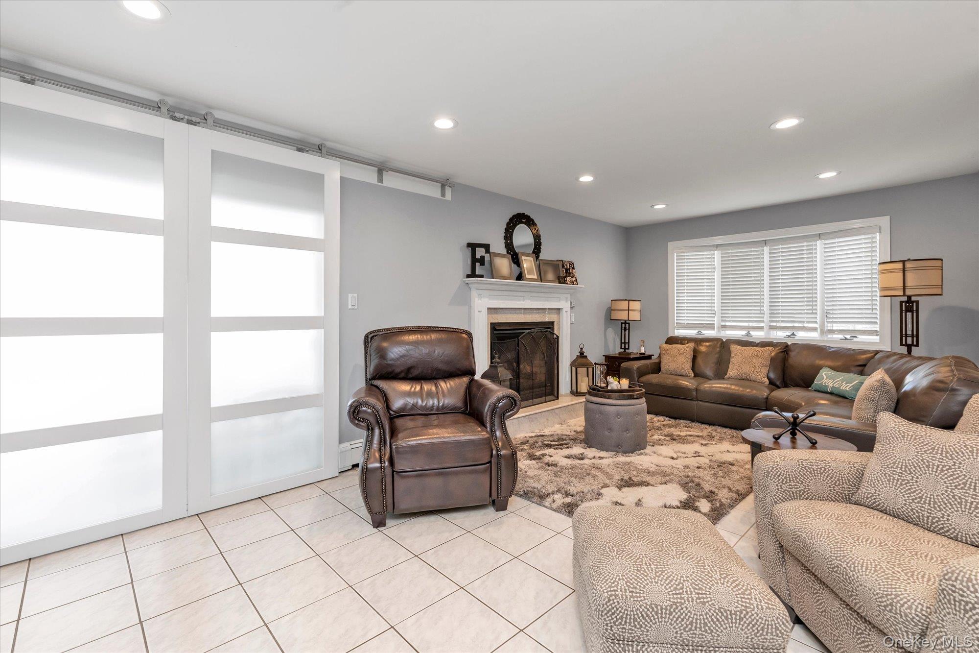 Furnished living room with a white fireplace, brown leather seating, and large frosted sliding doors.
