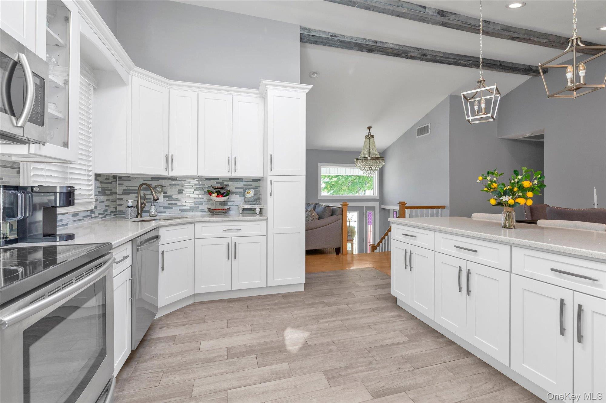 Bright kitchen with white cabinetry, stainless appliances, gray tile backsplash, and a large island.