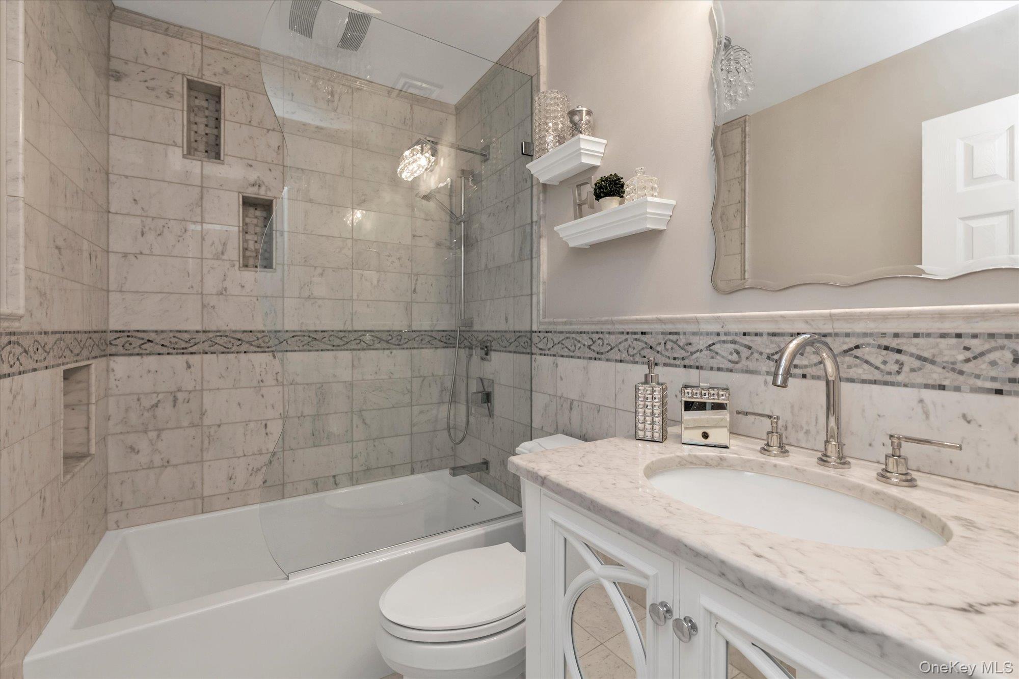 Bathroom with marble-look tile, a glass shower enclosure, and a white vanity.