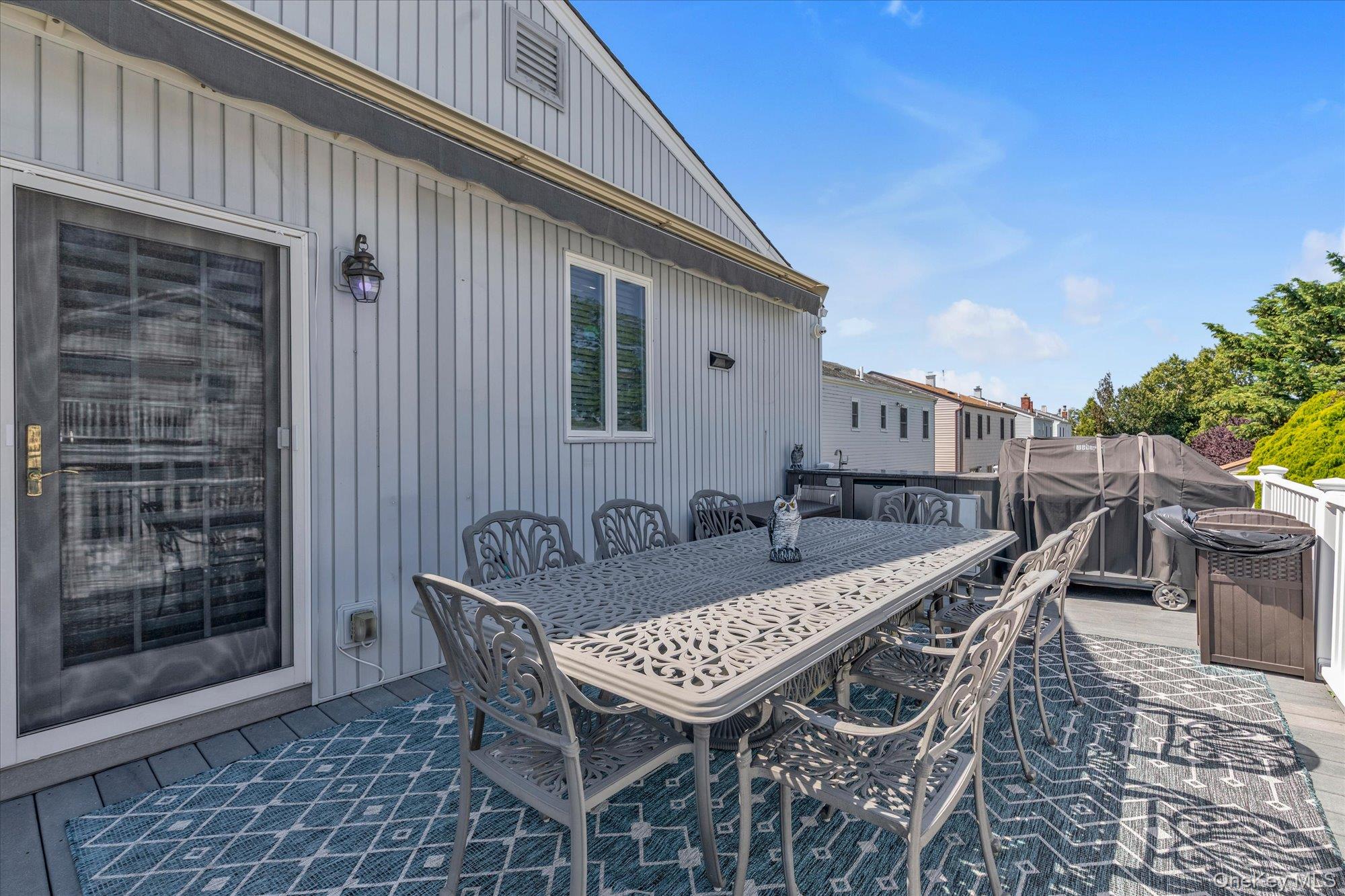 Outdoor deck with a metal dining set, patterned rug, covered grill, and white railing.