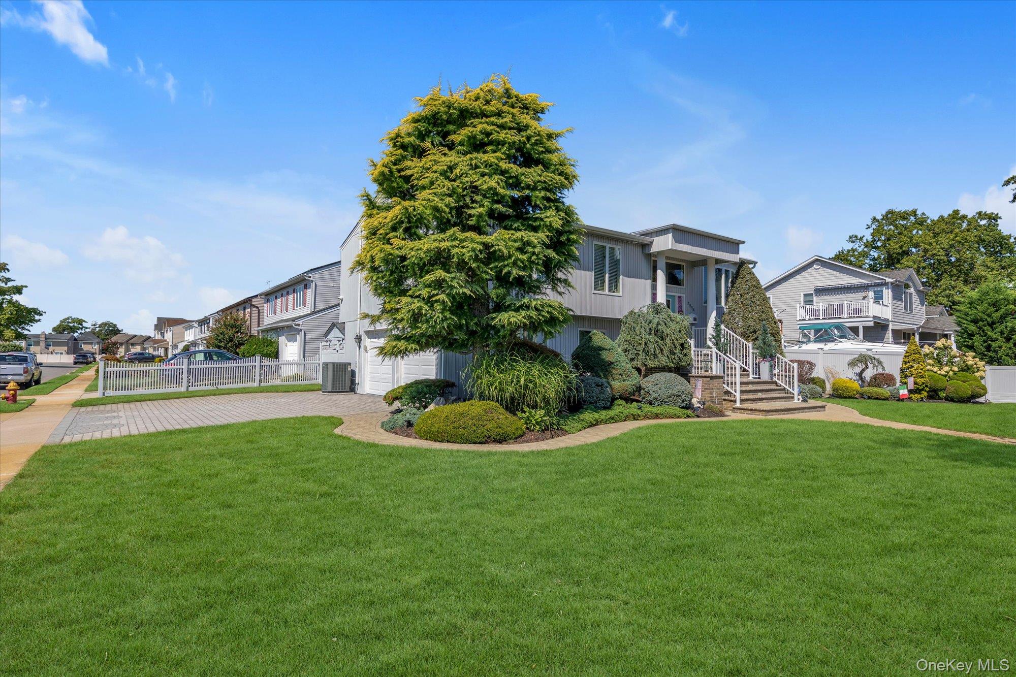 Gray two-story home with a broad green lawn, mature tree, landscaped beds, and front steps.