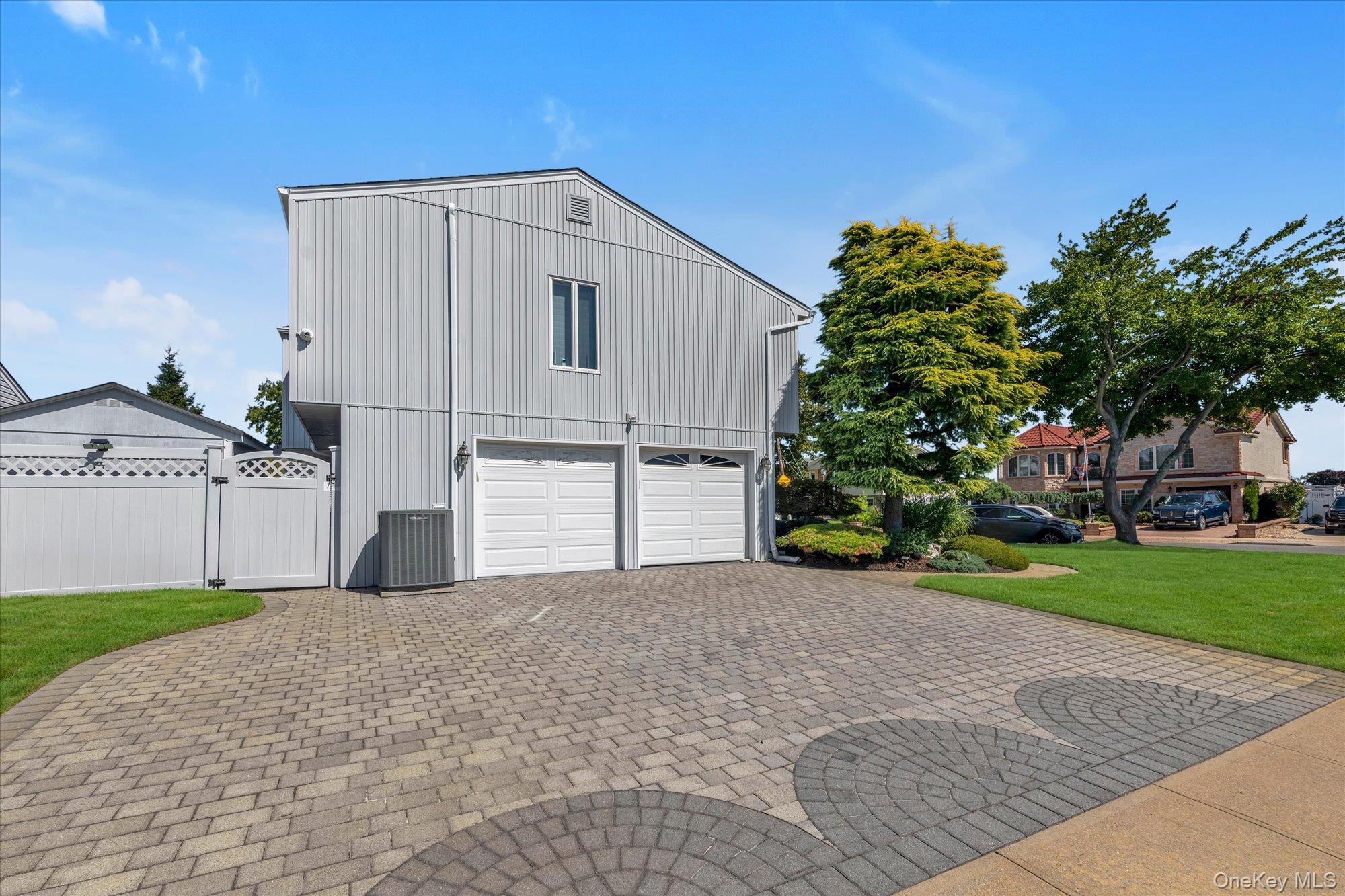 Two-story gray garage with two white doors and a broad patterned-paver driveway.