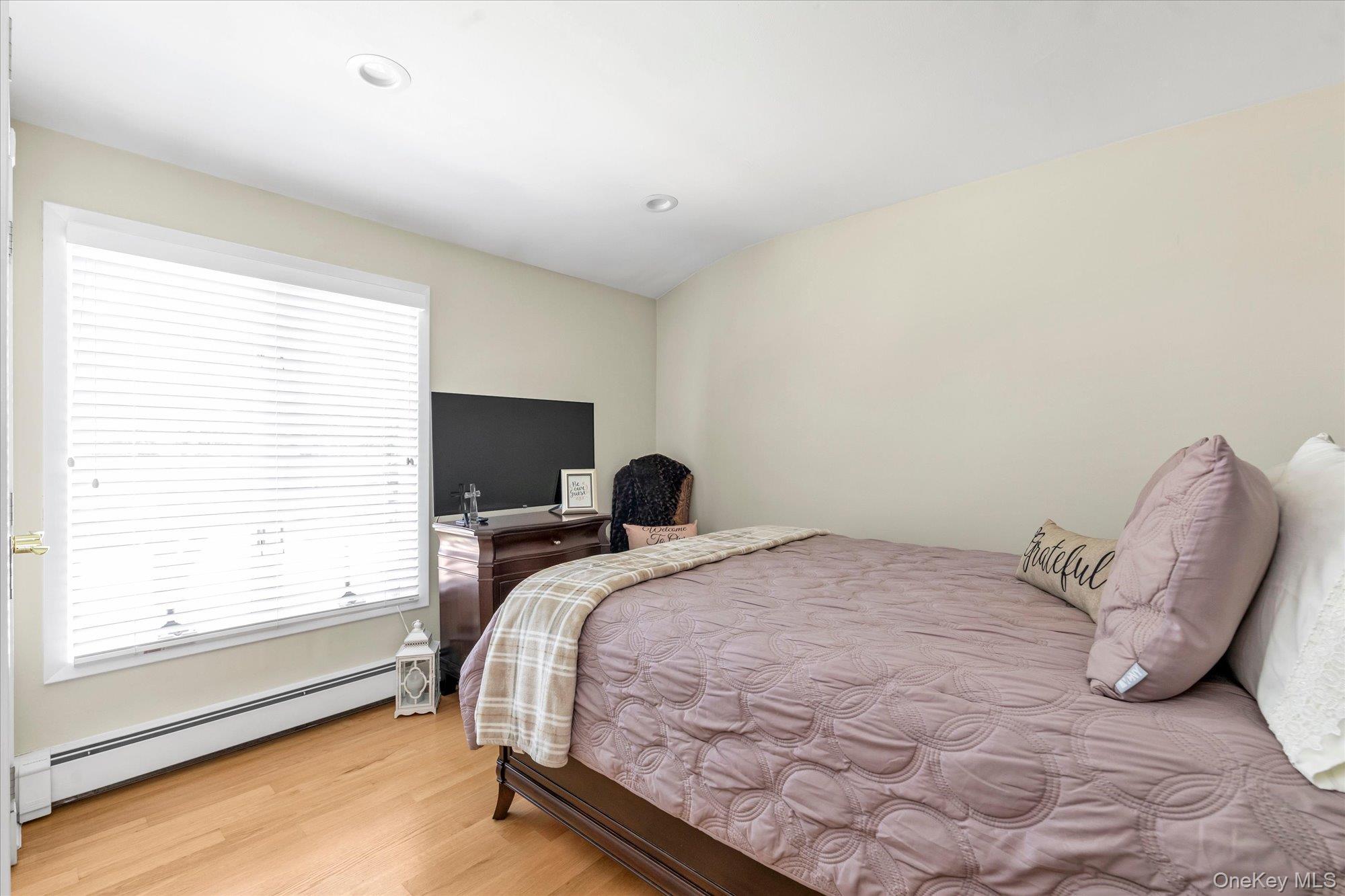 Bedroom with a mauve quilted bed, plaid throw, and large window with white blinds.