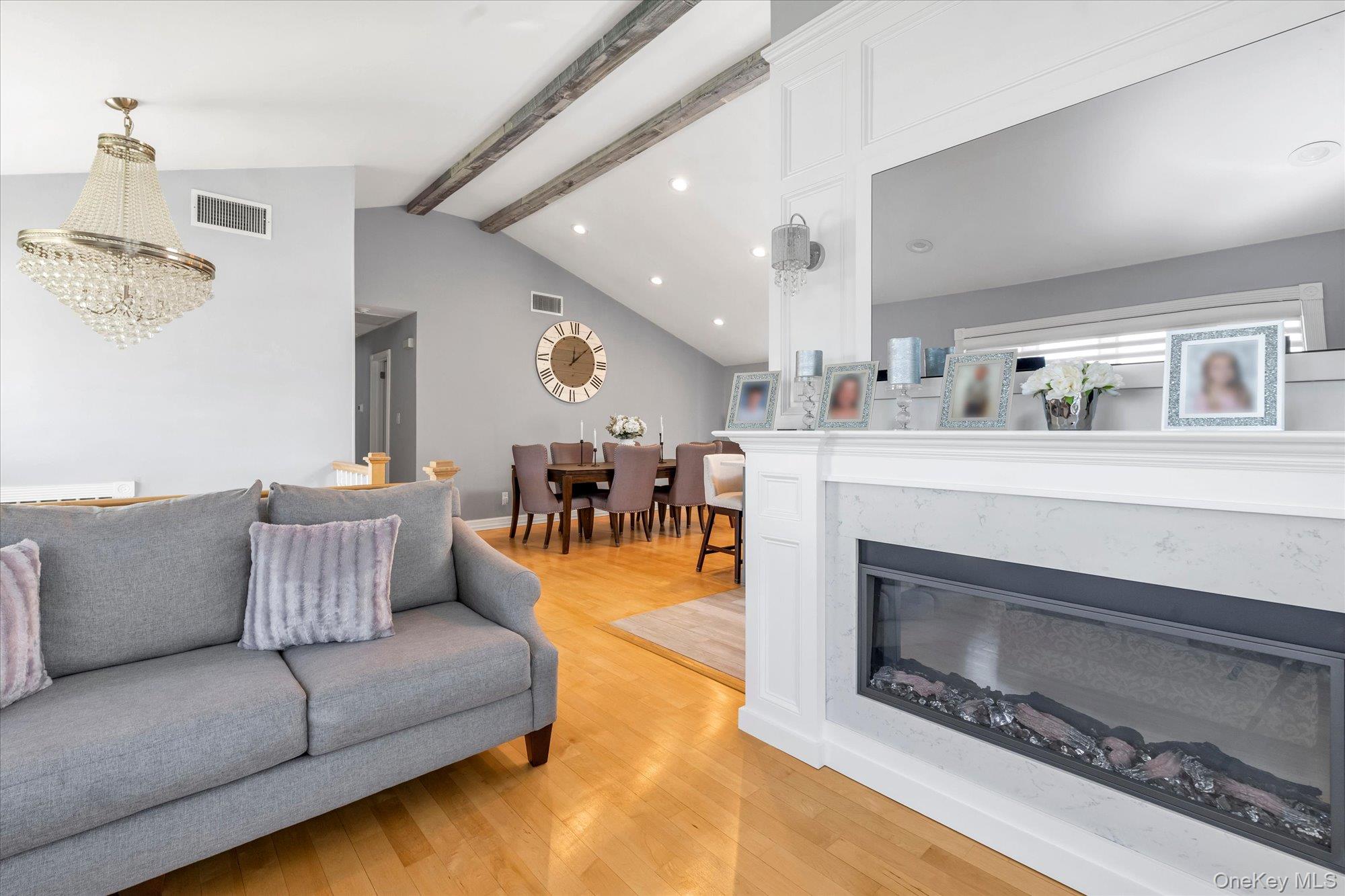 Living room with vaulted beamed ceiling, gray sofa, hardwood floors, and a white marble fireplace.