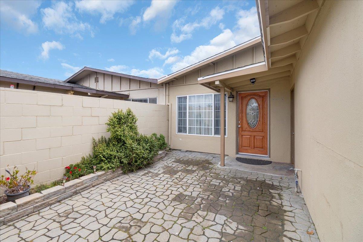 Home entrance with a covered porch, wooden glass-panel door, and stone-paved courtyard.