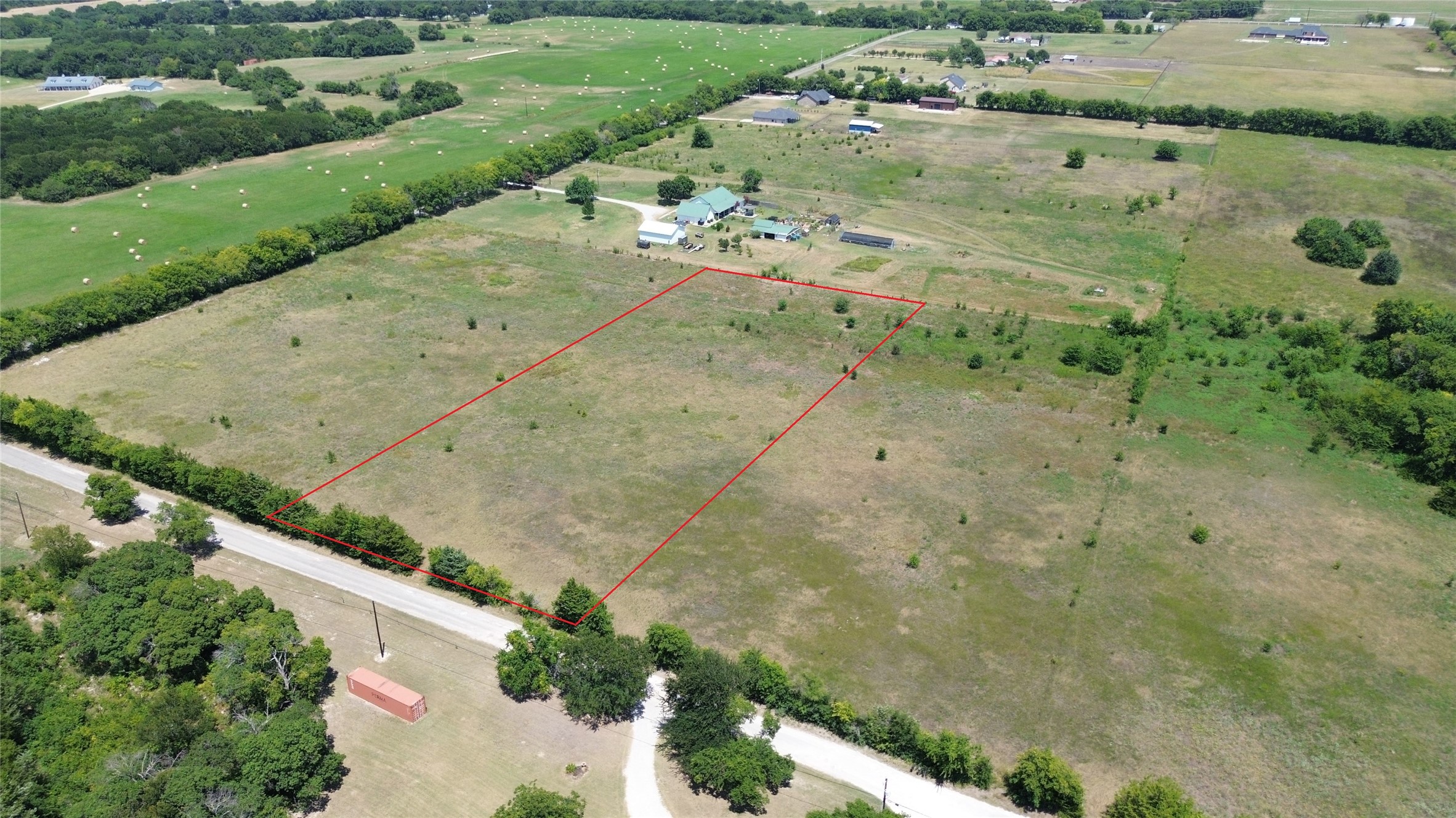 Aerial view of a rural parcel outlined in red beside a tree-lined road.