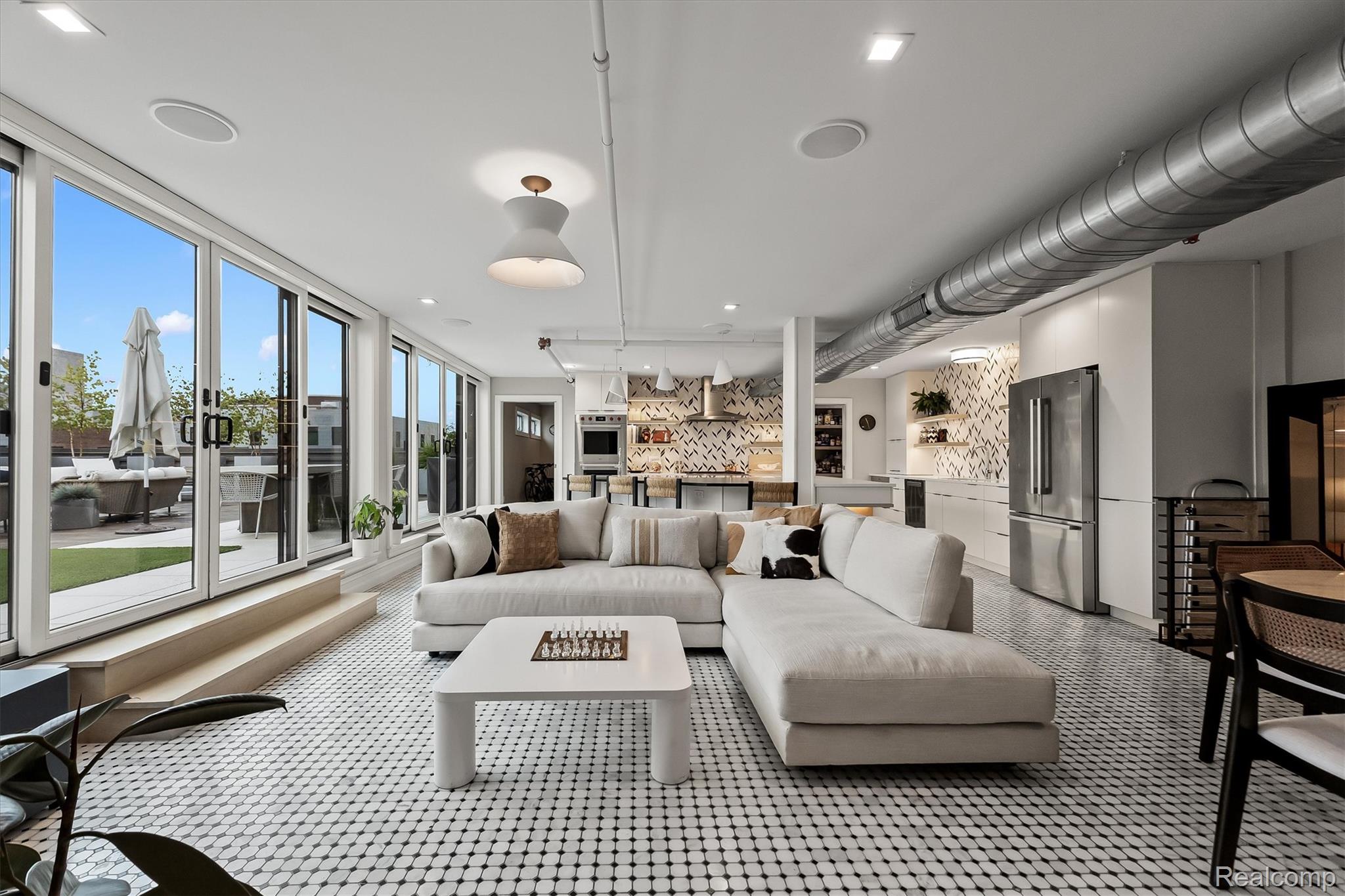 Open-plan living room and kitchen with a white sectional, patterned tile floor, and glass doors to a terrace.