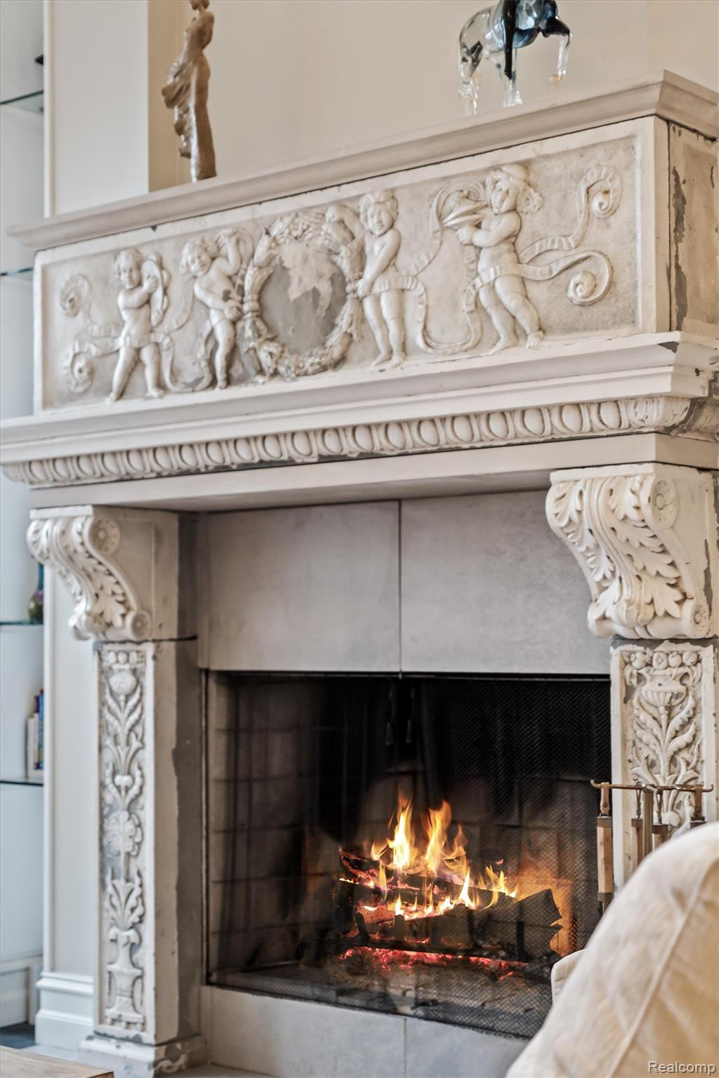 Lit fireplace with an ornate carved stone mantel and sculpted figures.